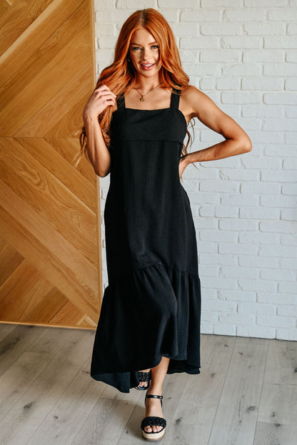 Front view of Nisha Black Maxi Dress, showing square neckline, sleeveless design, and ruffle high-low hem.