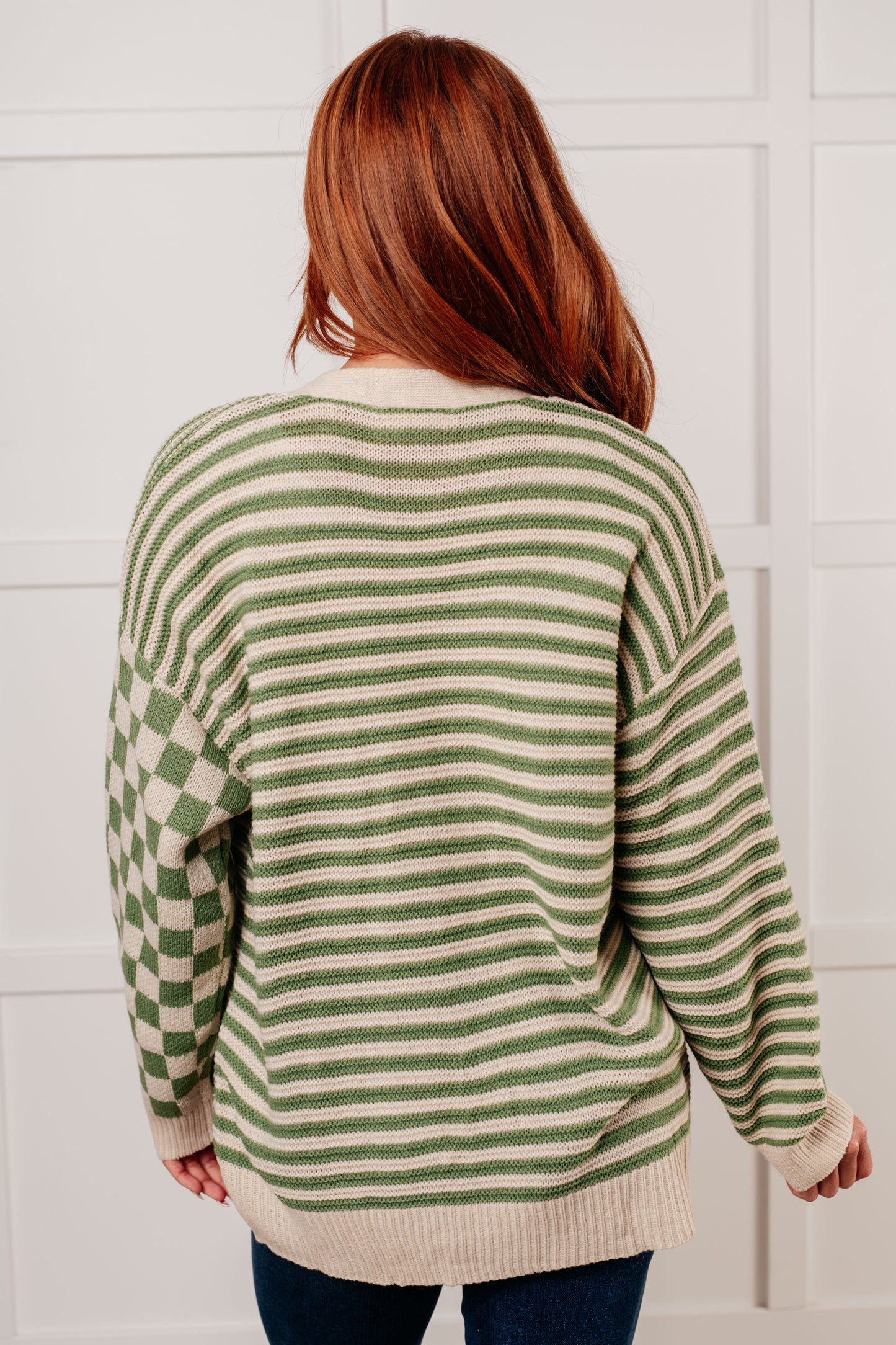 A green and beige check and stripe sweater knit cardigan with a V-neckline and long sleeves. The design features button closures, banded ribbed sleeve cuffs, and a ribbed hemline.