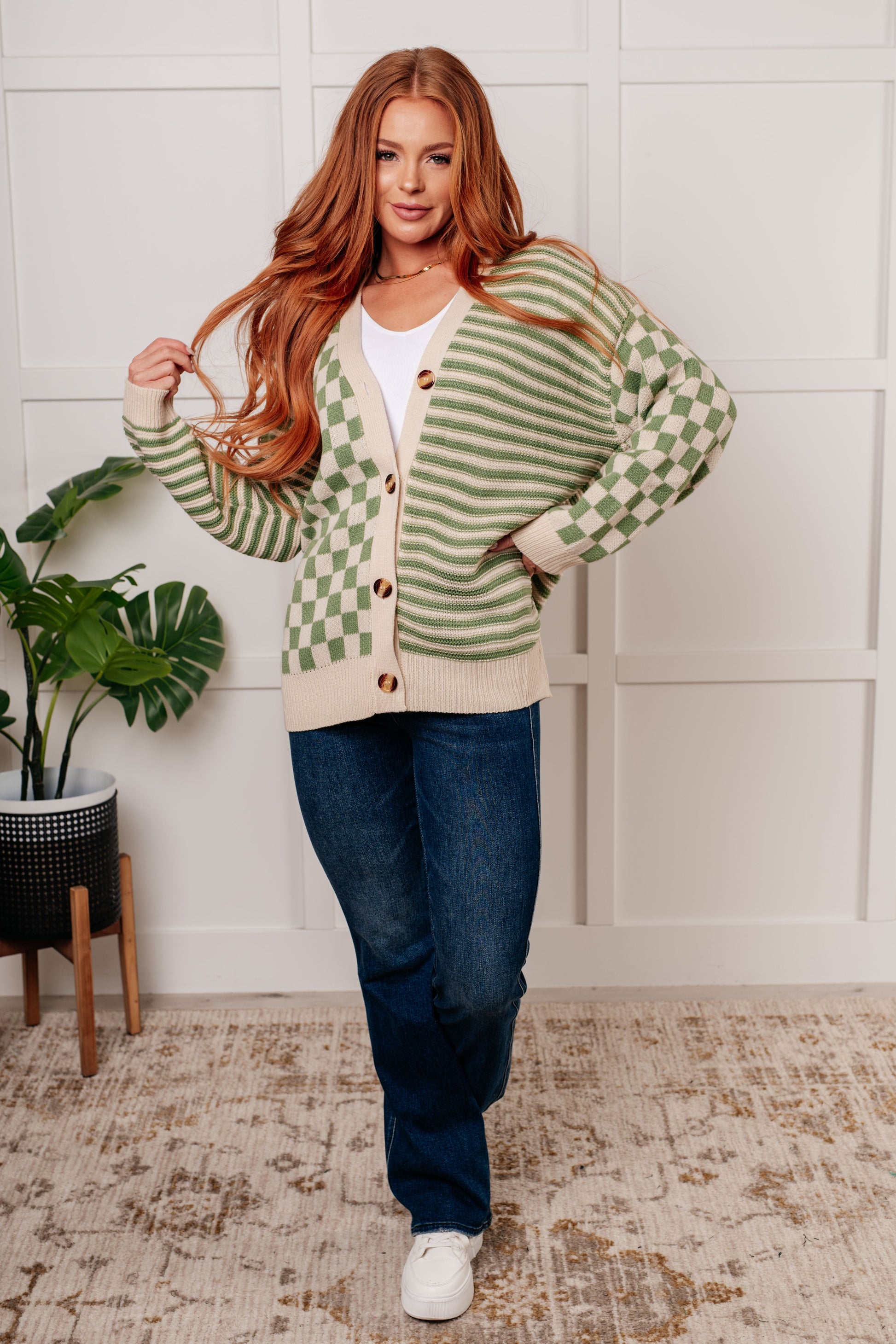 A green and beige check and stripe sweater knit cardigan with a V-neckline and long sleeves. The design features button closures, banded ribbed sleeve cuffs, and a ribbed hemline.