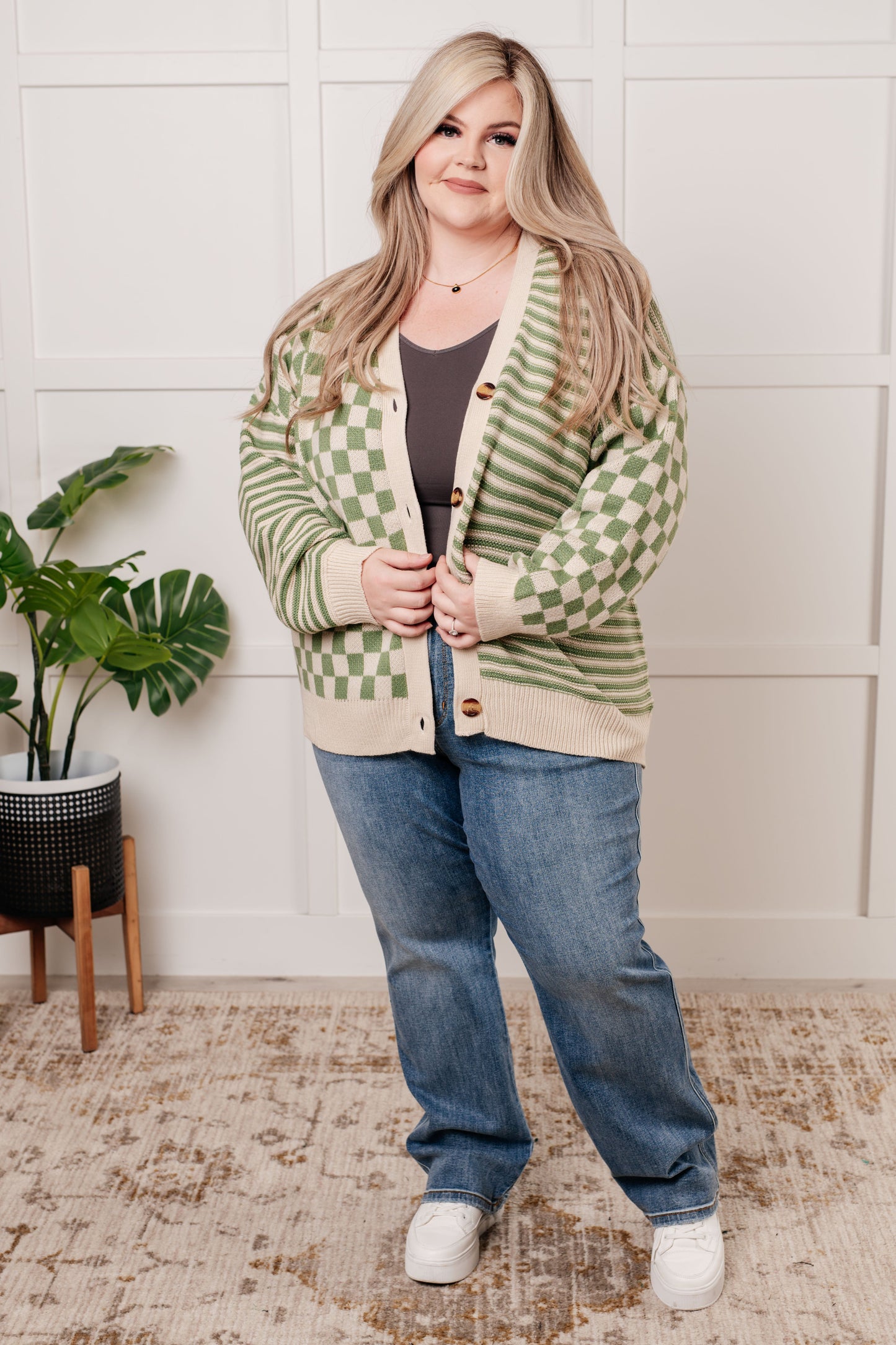 A green and beige check and stripe sweater knit cardigan with a V-neckline and long sleeves. The design features button closures, banded ribbed sleeve cuffs, and a ribbed hemline.