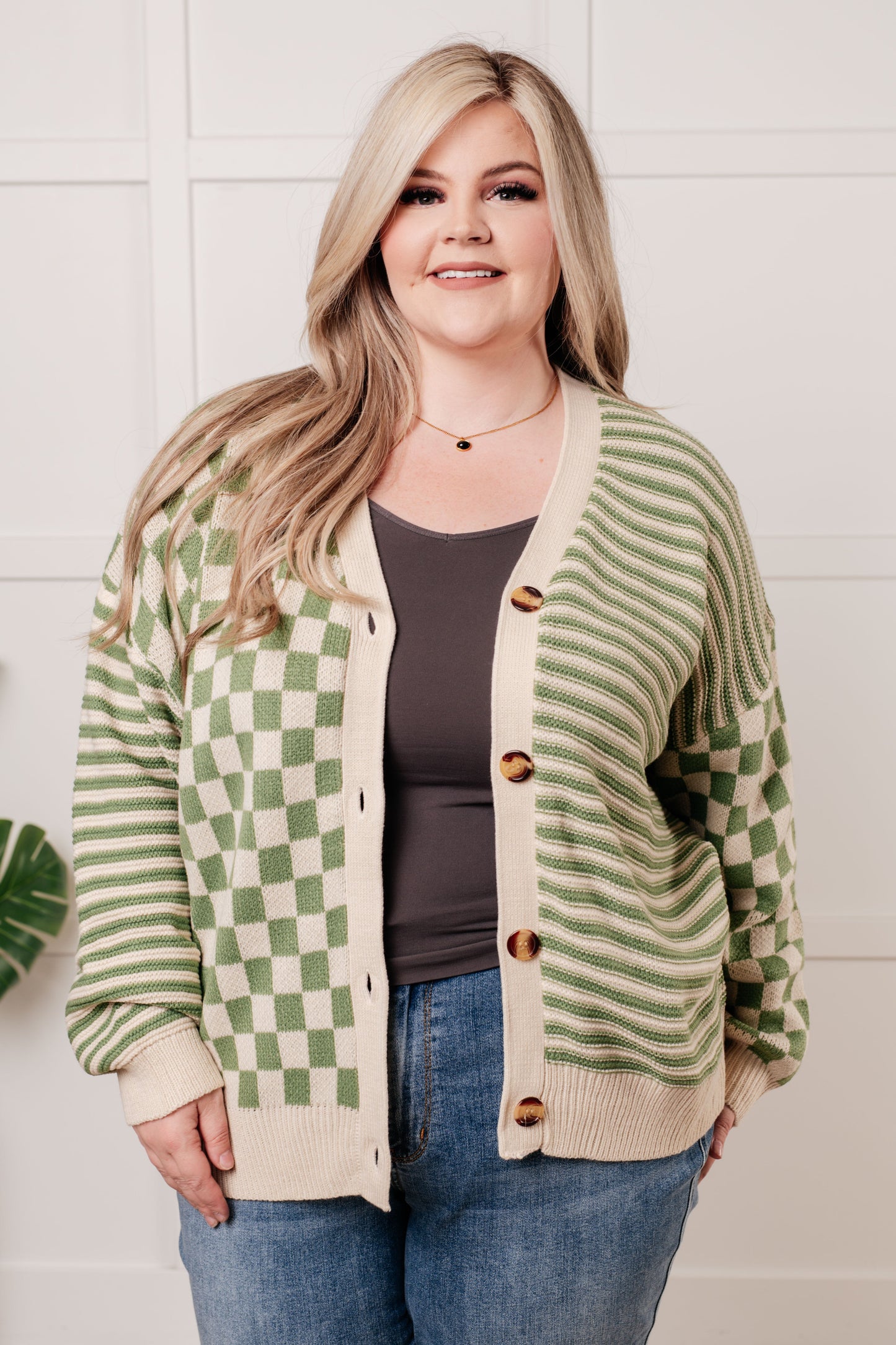 A green and beige check and stripe sweater knit cardigan with a V-neckline and long sleeves. The design features button closures, banded ribbed sleeve cuffs, and a ribbed hemline.