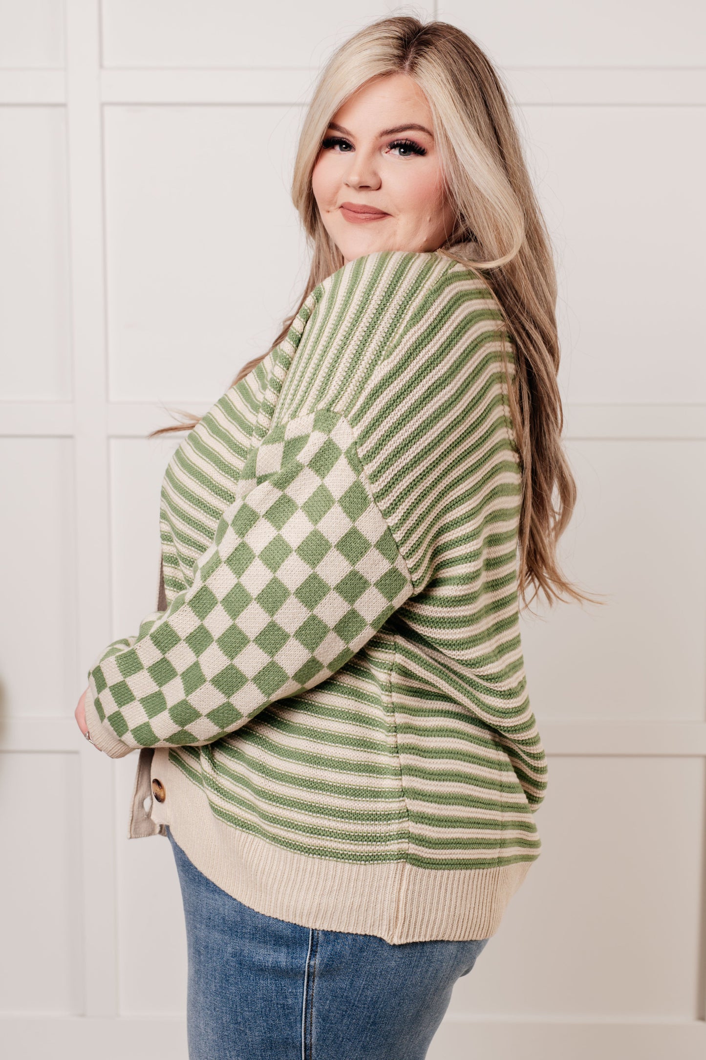 A green and beige check and stripe sweater knit cardigan with a V-neckline and long sleeves. The design features button closures, banded ribbed sleeve cuffs, and a ribbed hemline.