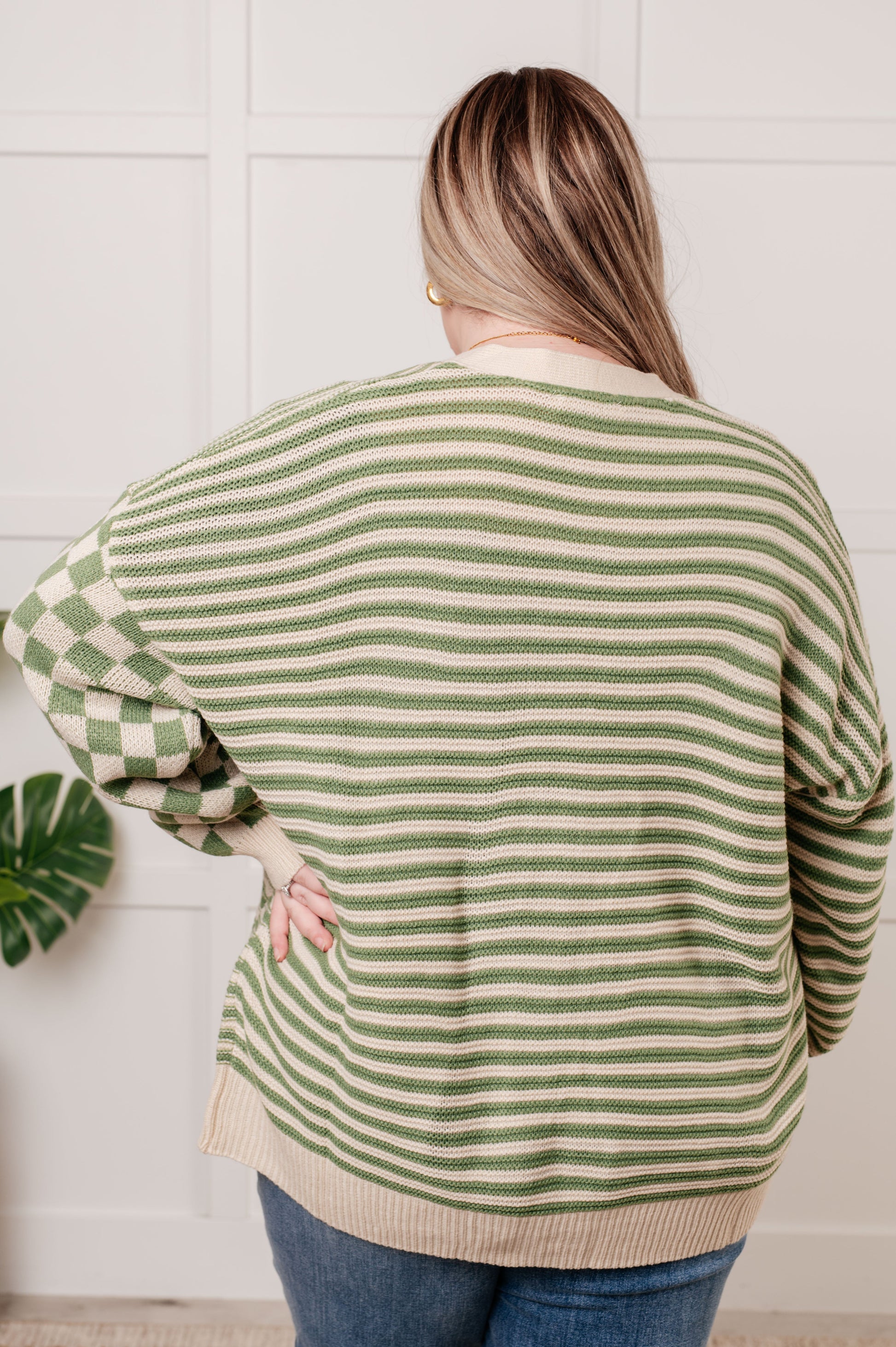 A green and beige check and stripe sweater knit cardigan with a V-neckline and long sleeves. The design features button closures, banded ribbed sleeve cuffs, and a ribbed hemline.