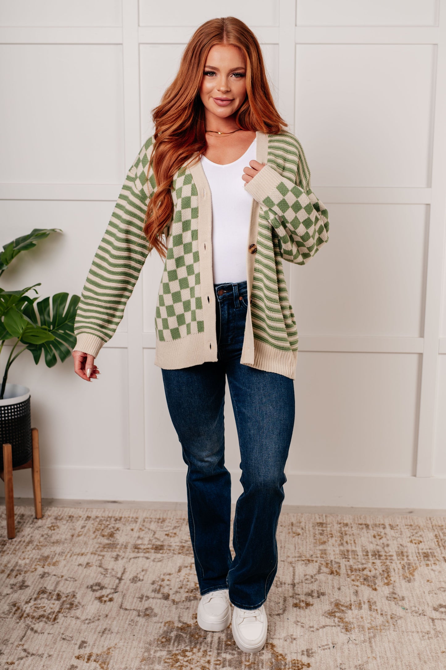 A green and beige check and stripe sweater knit cardigan with a V-neckline and long sleeves. The design features button closures, banded ribbed sleeve cuffs, and a ribbed hemline.