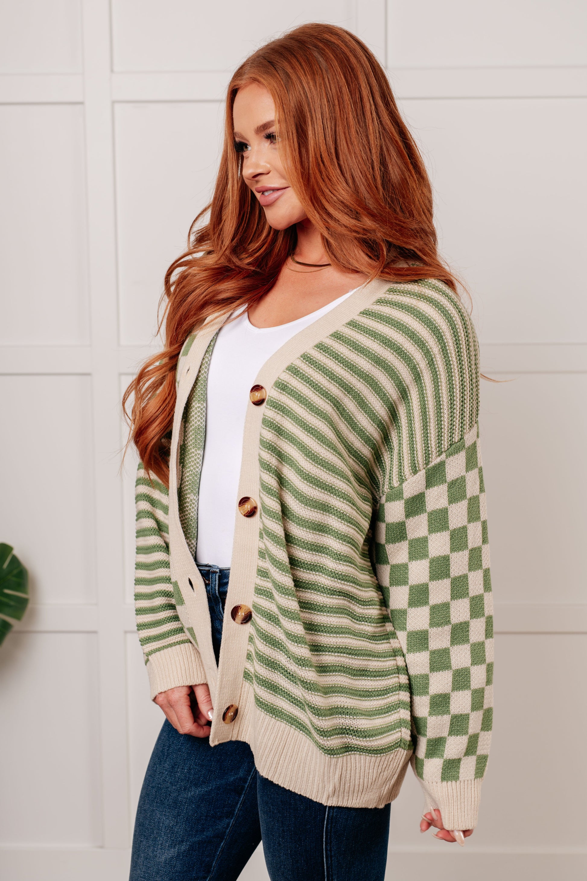 A green and beige check and stripe sweater knit cardigan with a V-neckline and long sleeves. The design features button closures, banded ribbed sleeve cuffs, and a ribbed hemline.