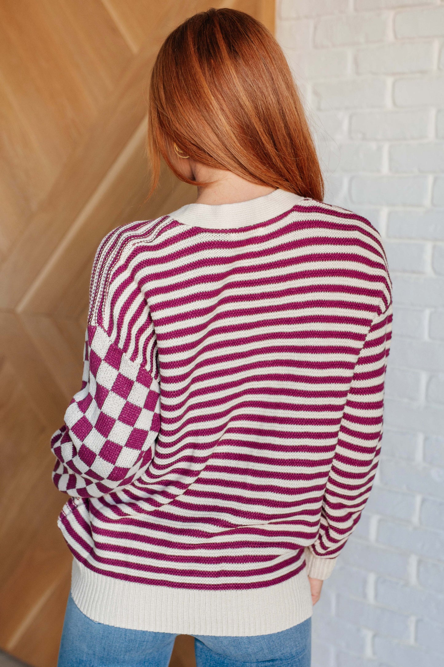 Back view of women's pink and beige cardigan featuring a checkered and striped pattern, V-neckline, and long sleeves. Designed with button closures, banded ribbed cuffs, and a ribbed hemline.