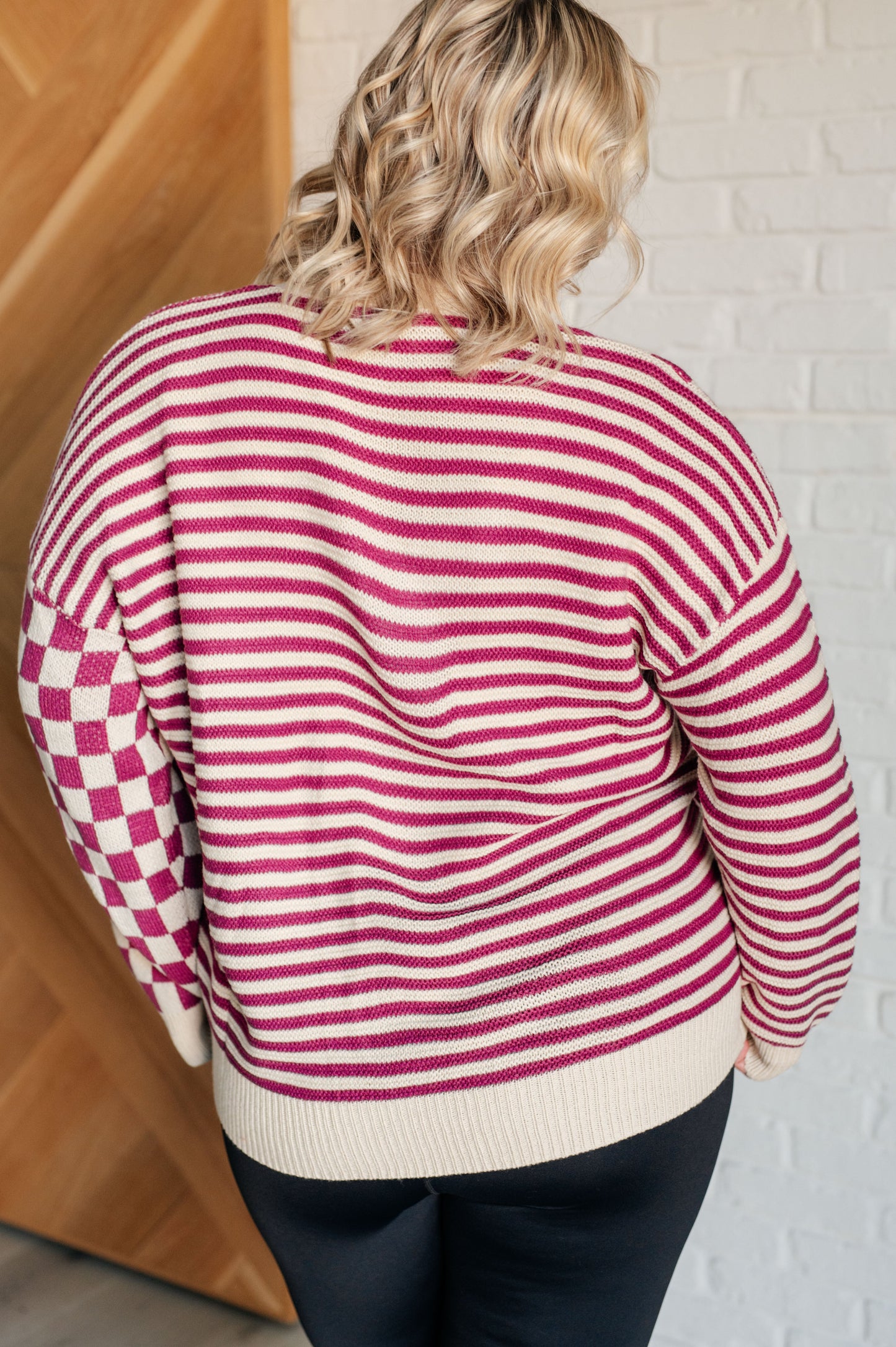 Back view of women's pink and beige cardigan featuring a checkered and striped pattern, V-neckline, and long sleeves. Designed with button closures, banded ribbed cuffs, and a ribbed hemline.