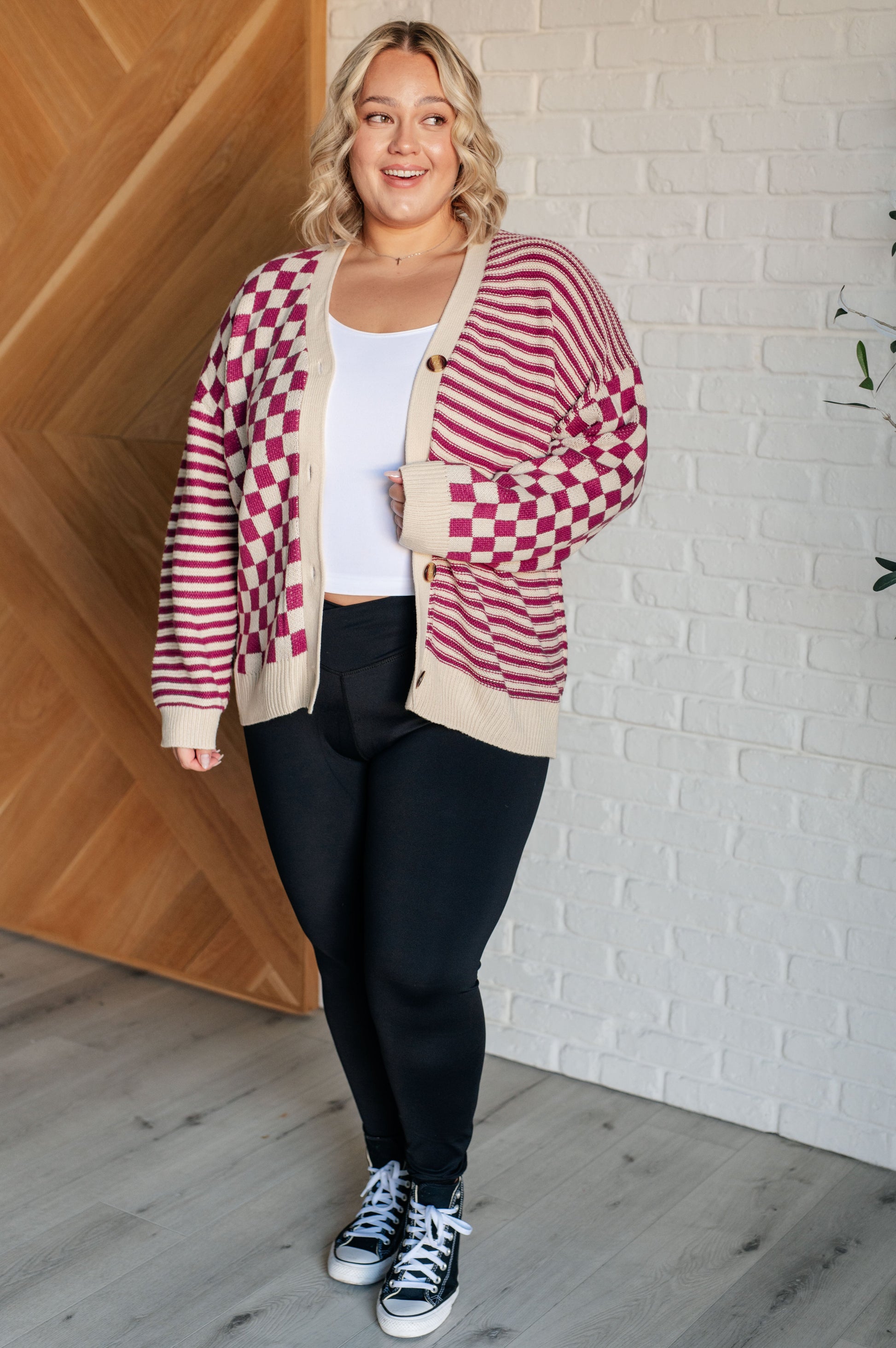 Women's pink and beige cardigan featuring a checkered and striped pattern, V-neckline, and long sleeves. Designed with button closures, banded ribbed cuffs, and a ribbed hemline.