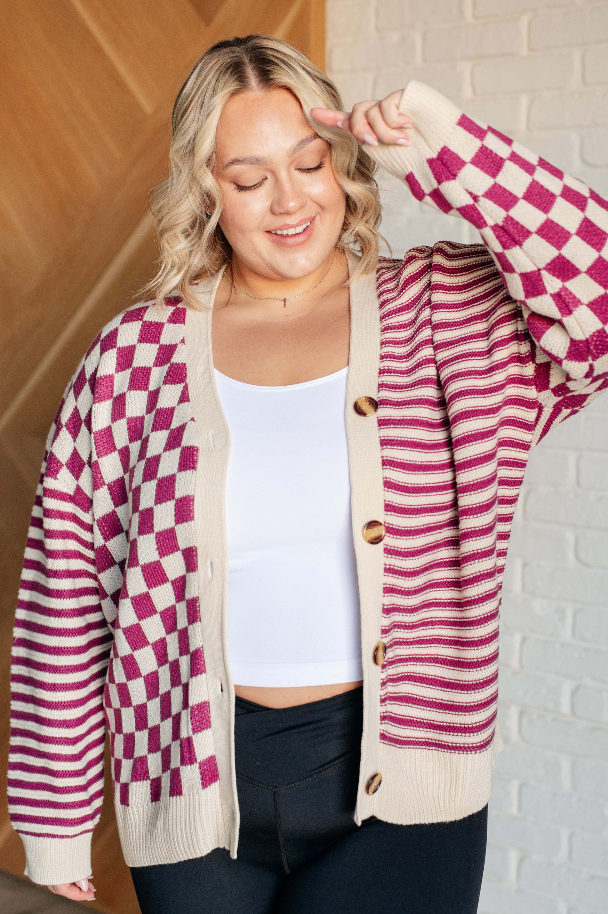 Women's pink and beige cardigan featuring a checkered and striped pattern, V-neckline, and long sleeves. Designed with button closures, banded ribbed cuffs, and a ribbed hemline.