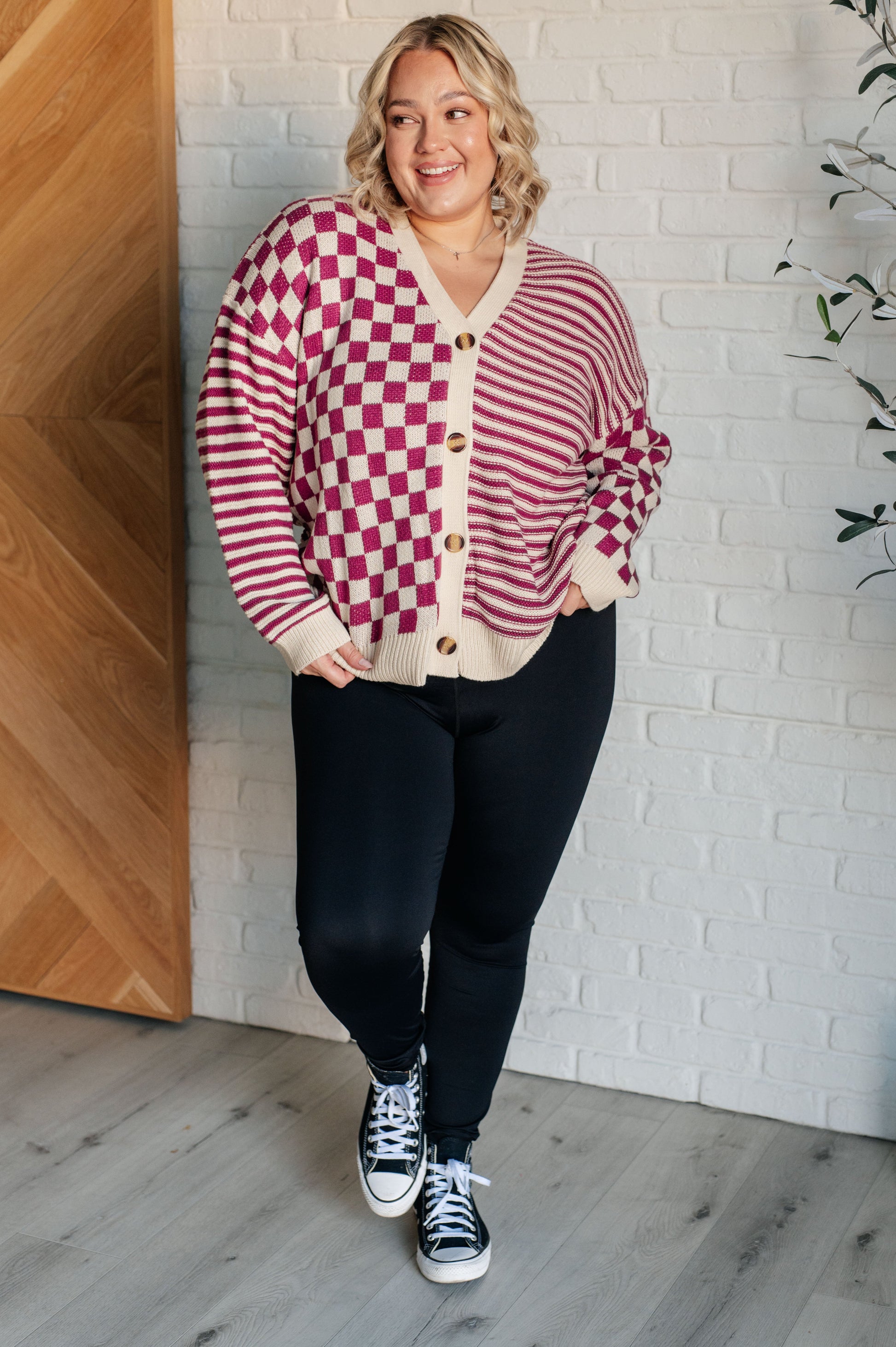 Women's pink and beige cardigan featuring a checkered and striped pattern, V-neckline, and long sleeves. Designed with button closures, banded ribbed cuffs, and a ribbed hemline.