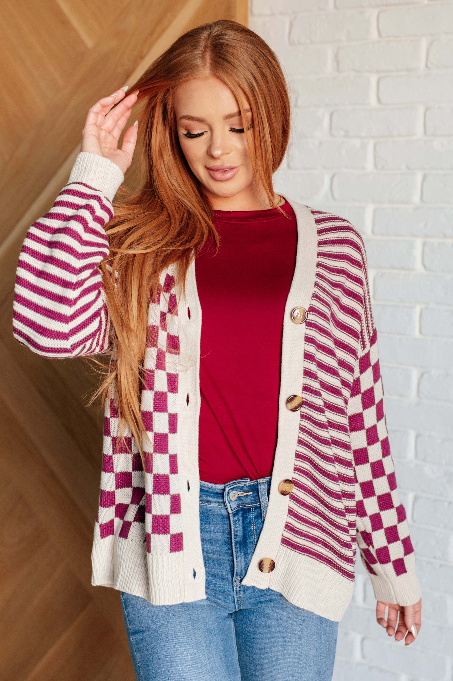 Women's pink and beige cardigan featuring a checkered and striped pattern, V-neckline, and long sleeves. Designed with button closures, banded ribbed cuffs, and a ribbed hemline.