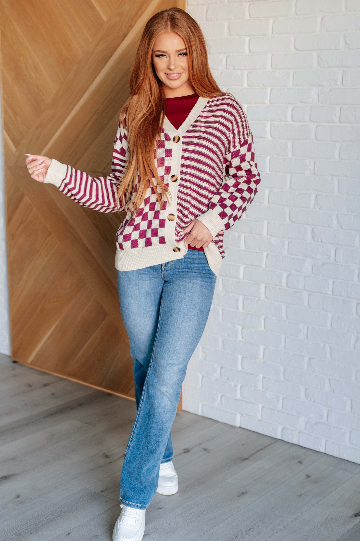 Women's pink and beige cardigan featuring a checkered and striped pattern, V-neckline, and long sleeves. Designed with button closures, banded ribbed cuffs, and a ribbed hemline.