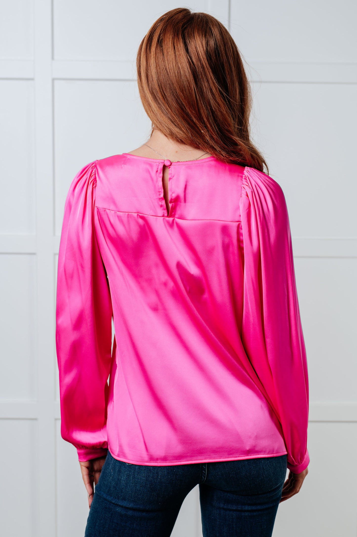 Pink poly satin blouse with round neckline and long puff sleeves. Features banded sleeve cuffs and a back keyhole button closure.