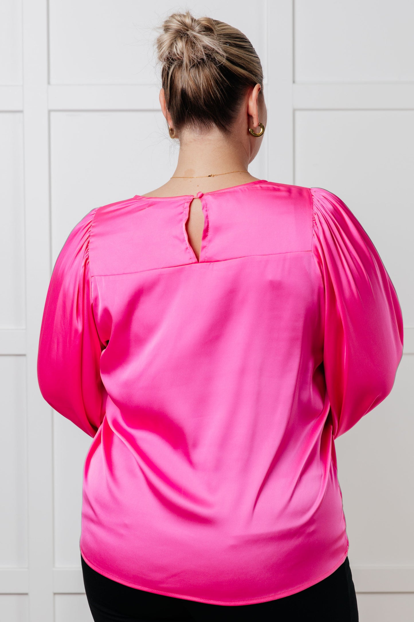 Pink poly satin blouse with round neckline and long puff sleeves. Features banded sleeve cuffs and a back keyhole button closure.