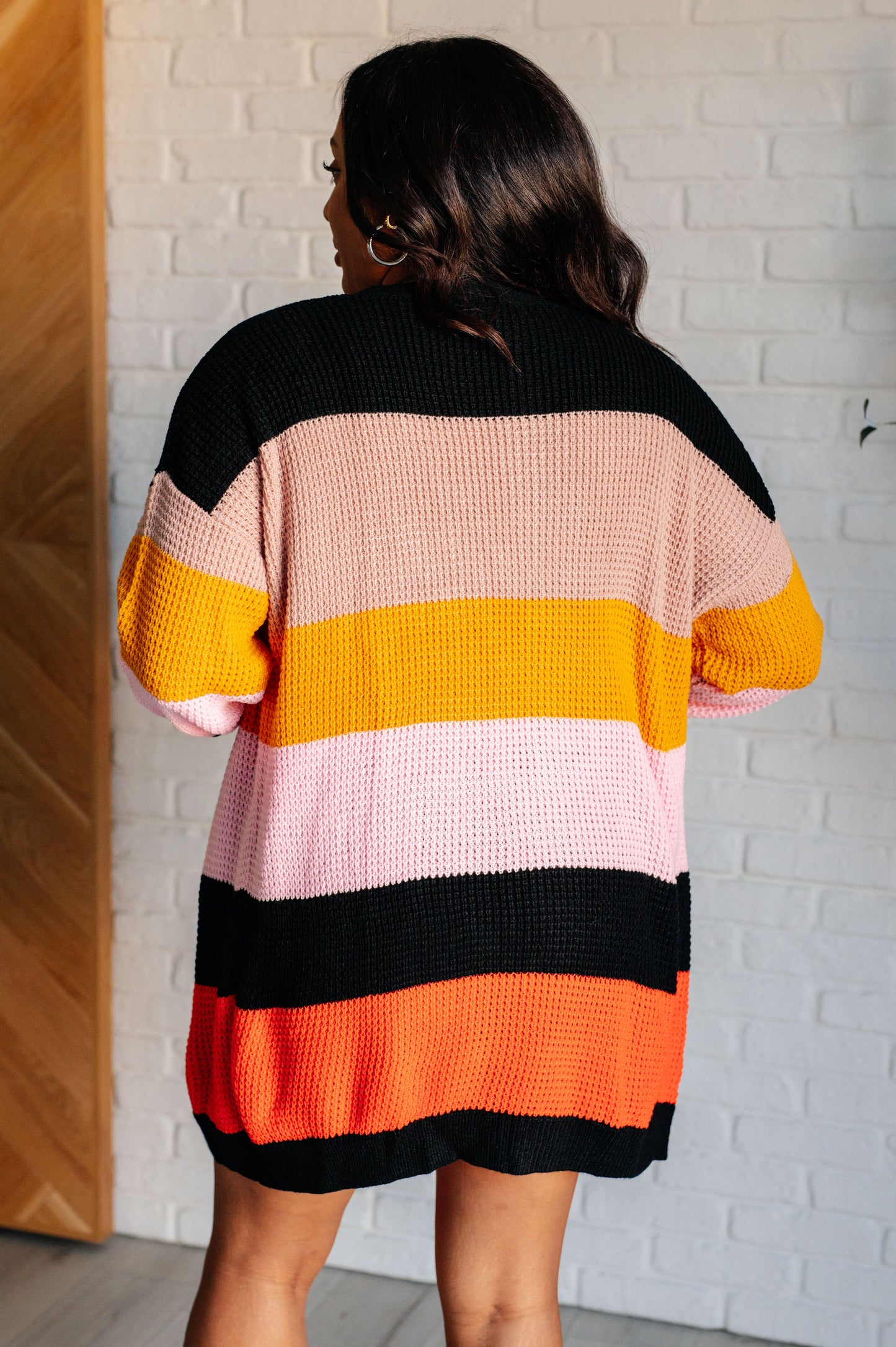 Striped open-front sweater with a cozy knit fabric featuring beige, pink, yellow, black, and orange stripes. Designed with long drop-shoulder sleeves and banded ribbed cuffs and hemline for a relaxed fit.