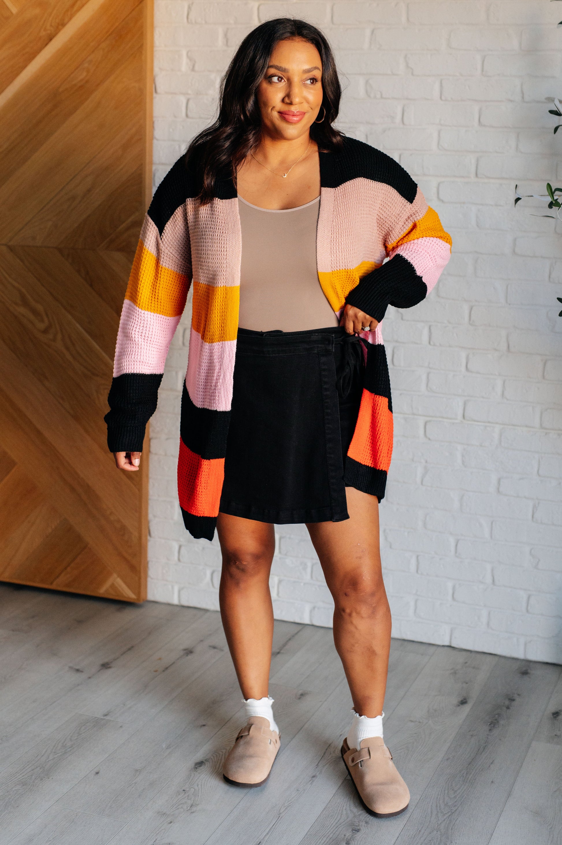 Striped open-front sweater with a cozy knit fabric featuring beige, pink, yellow, black, and orange stripes. Designed with long drop-shoulder sleeves and banded ribbed cuffs and hemline for a relaxed fit.