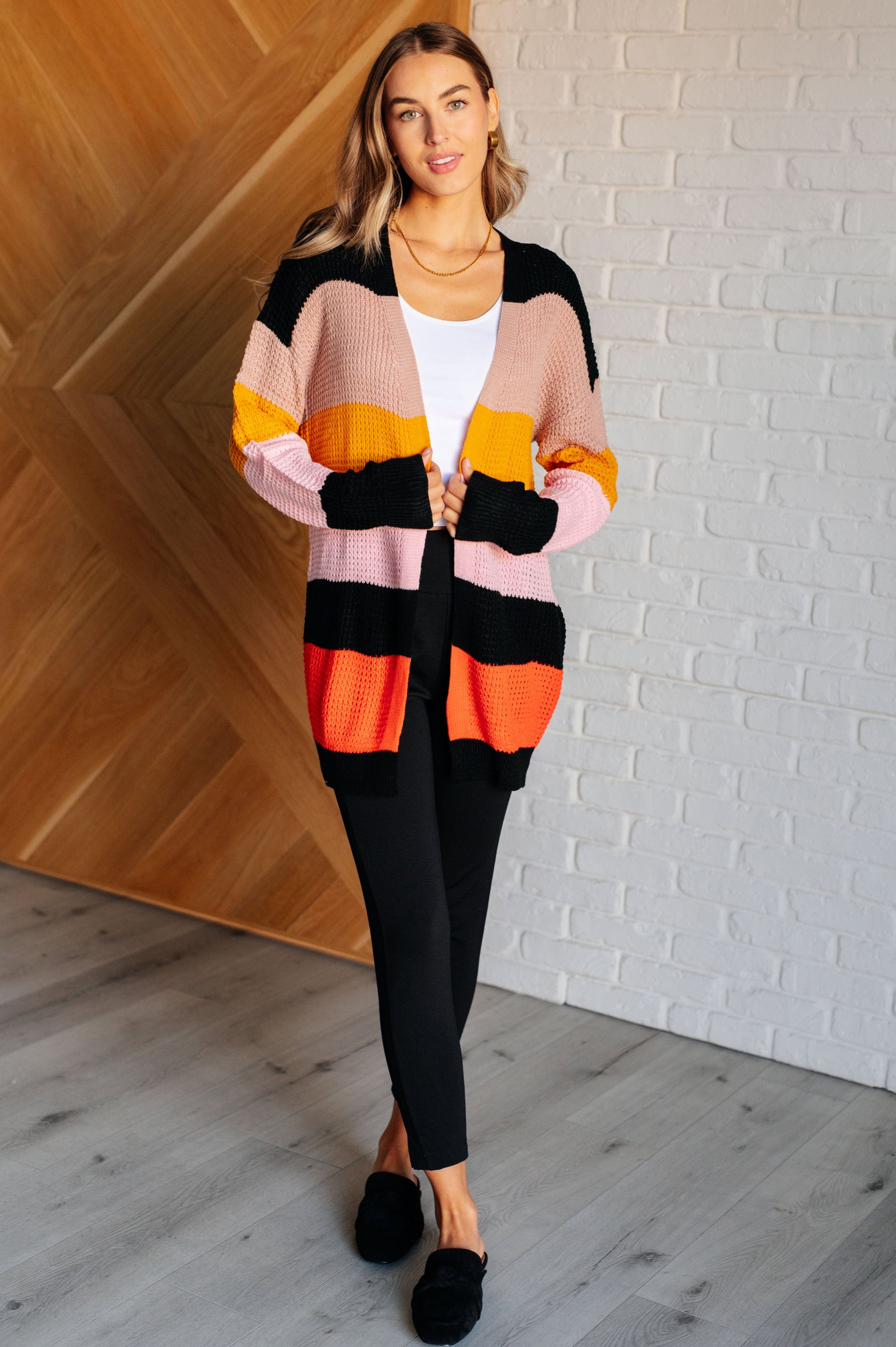 Striped open-front sweater with a cozy knit fabric featuring beige, pink, yellow, black, and orange stripes. Designed with long drop-shoulder sleeves and banded ribbed cuffs and hemline for a relaxed fit.