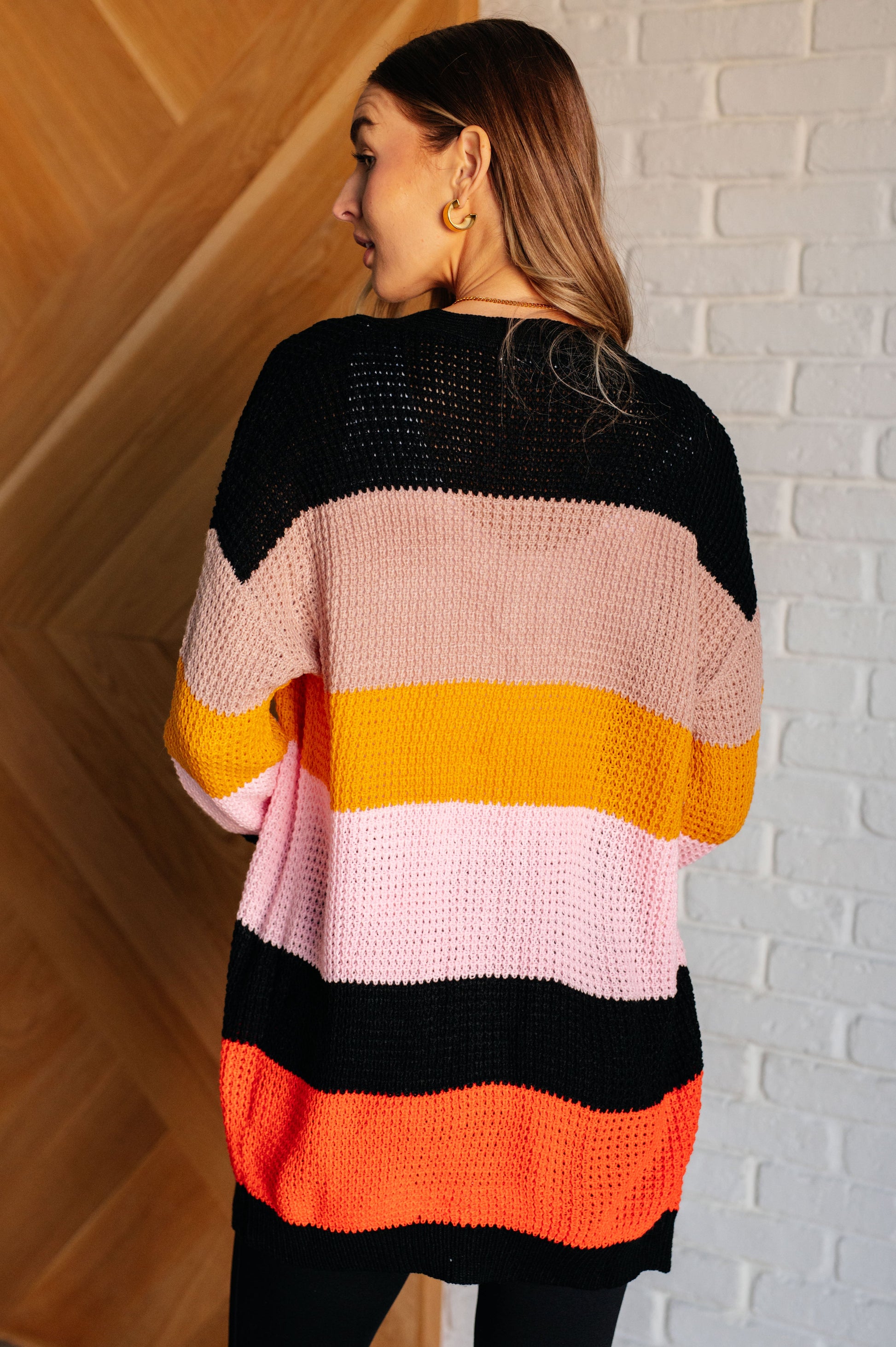 Striped open-front sweater with a cozy knit fabric featuring beige, pink, yellow, black, and orange stripes. Designed with long drop-shoulder sleeves and banded ribbed cuffs and hemline for a relaxed fit.