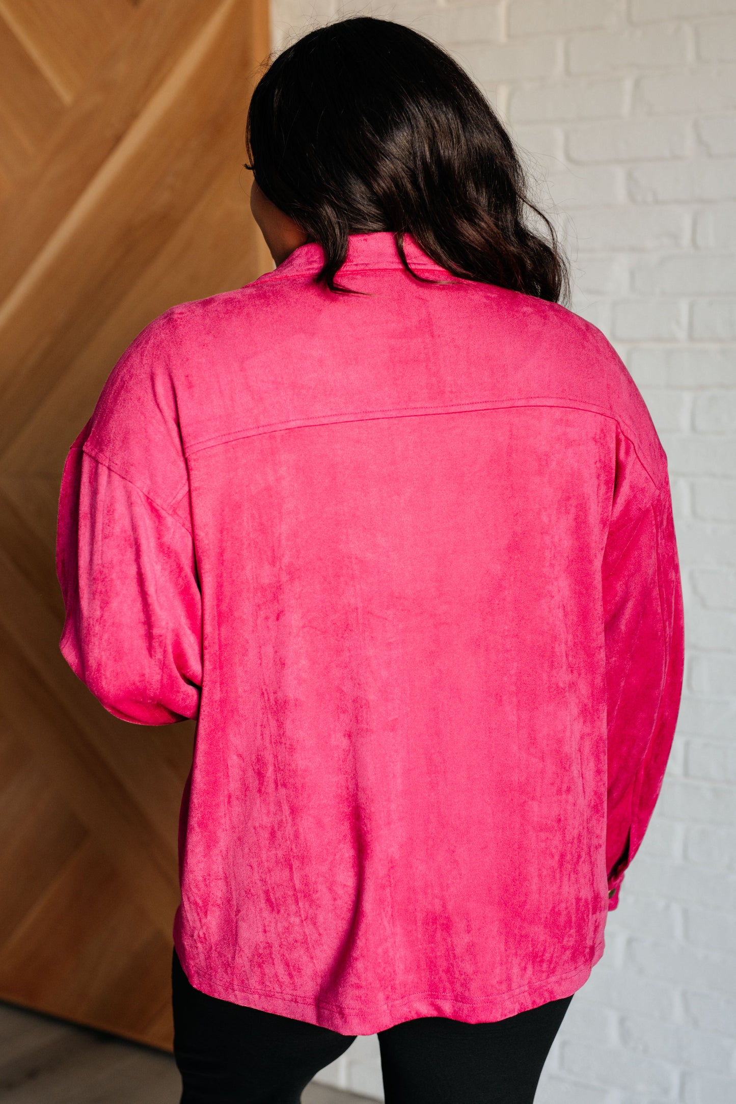 Vibrant pink faux suede button-down shirt with a collared neckline, drop shoulders, and long sleeves. Features snap button closures, cuffed sleeves, and chest flap pockets.