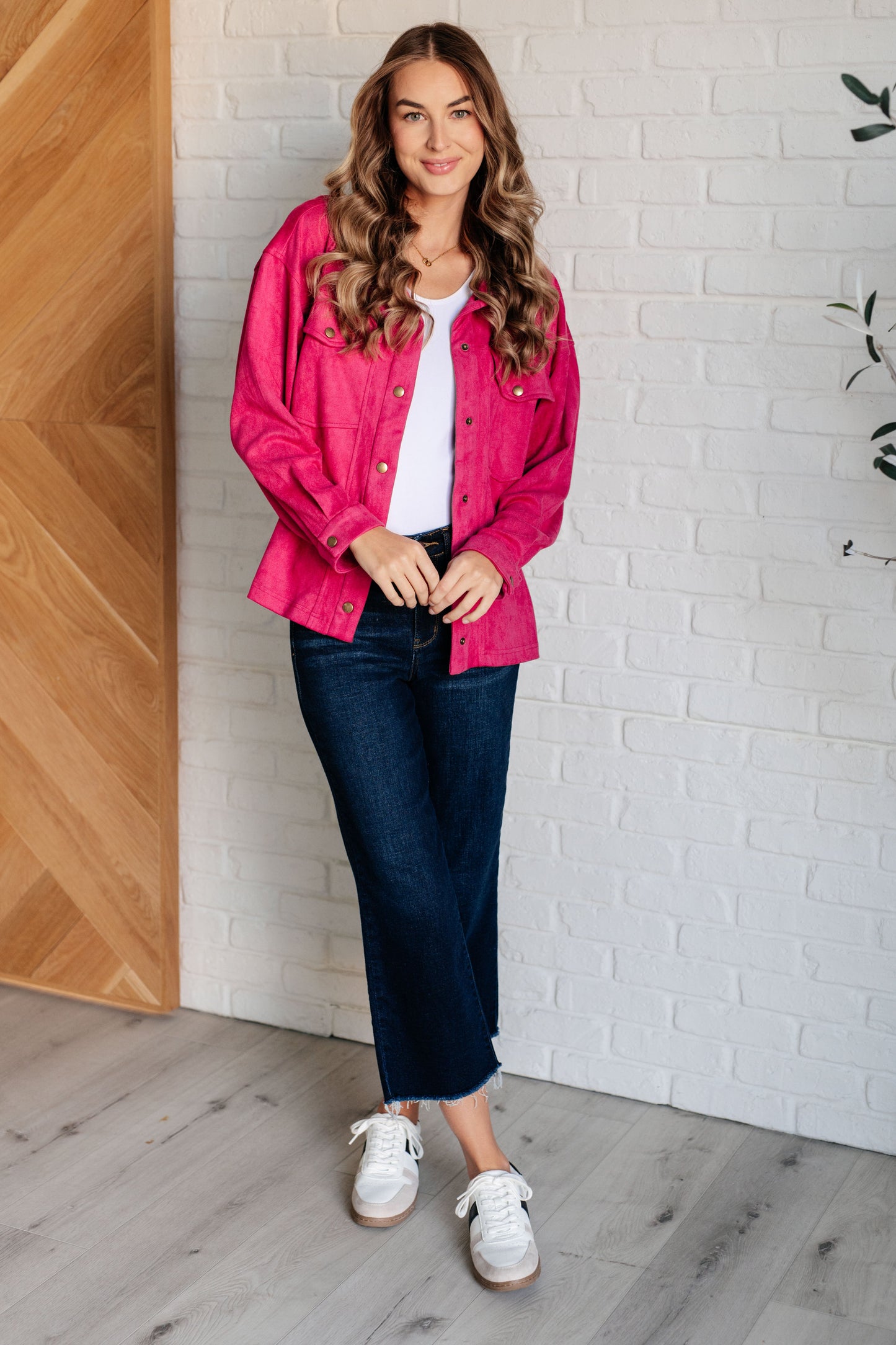 Vibrant pink faux suede button-down shirt with a collared neckline, drop shoulders, and long sleeves. Features snap button closures, cuffed sleeves, and chest flap pockets.