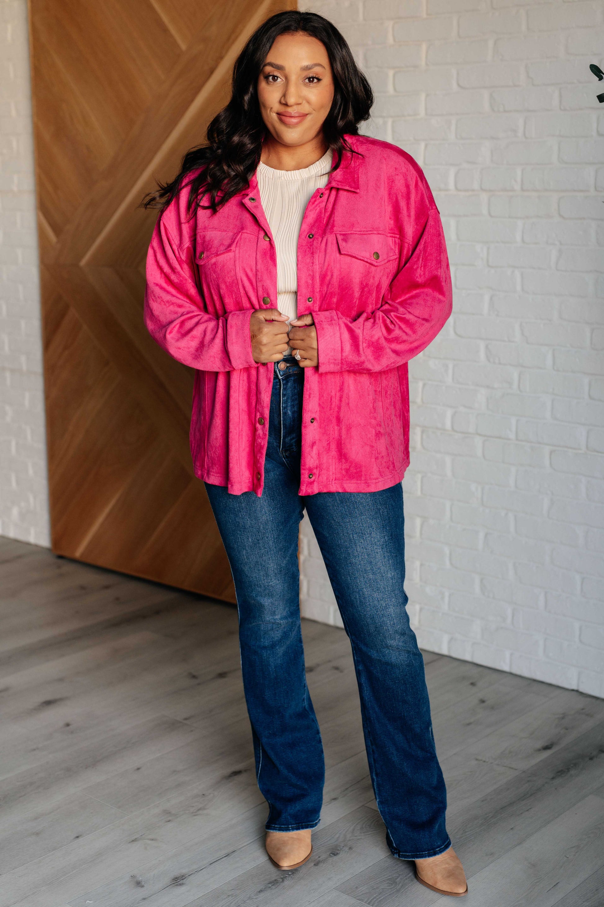 Vibrant pink faux suede button-down shirt with a collared neckline, drop shoulders, and long sleeves. Features snap button closures, cuffed sleeves, and chest flap pockets.