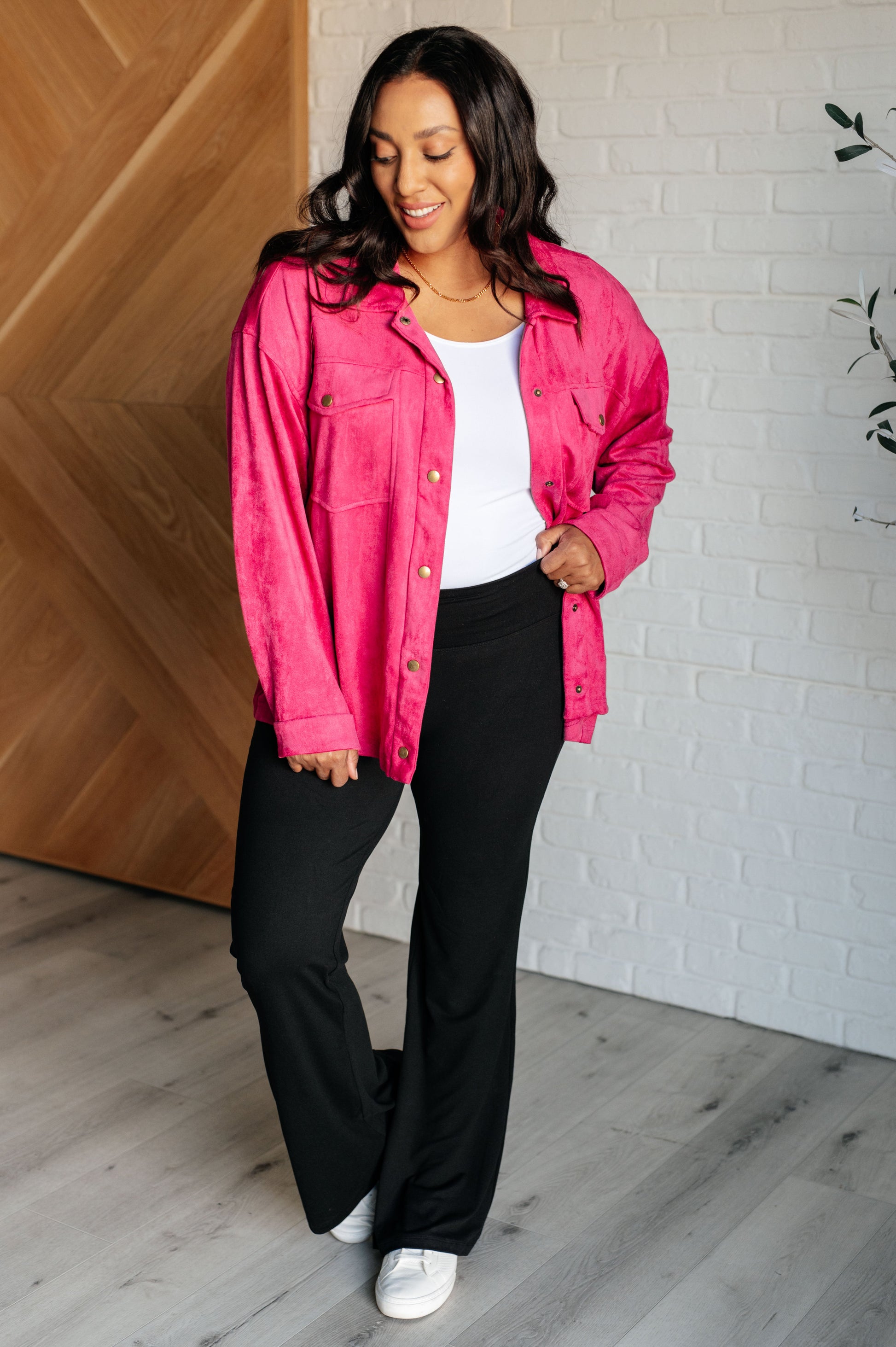 Vibrant pink faux suede button-down shirt with a collared neckline, drop shoulders, and long sleeves. Features snap button closures, cuffed sleeves, and chest flap pockets.