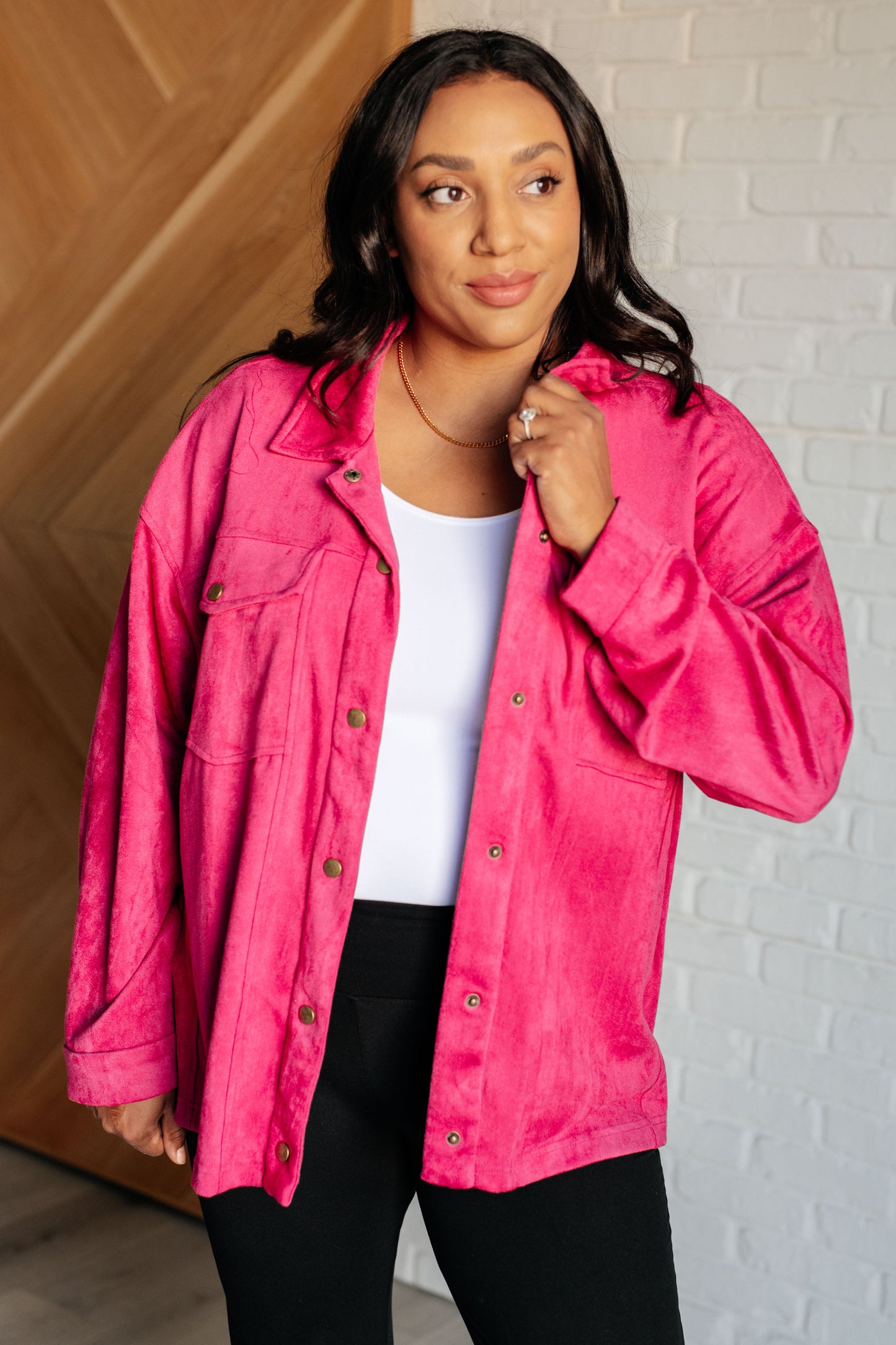 Vibrant pink faux suede button-down shirt with a collared neckline, drop shoulders, and long sleeves. Features snap button closures, cuffed sleeves, and chest flap pockets.