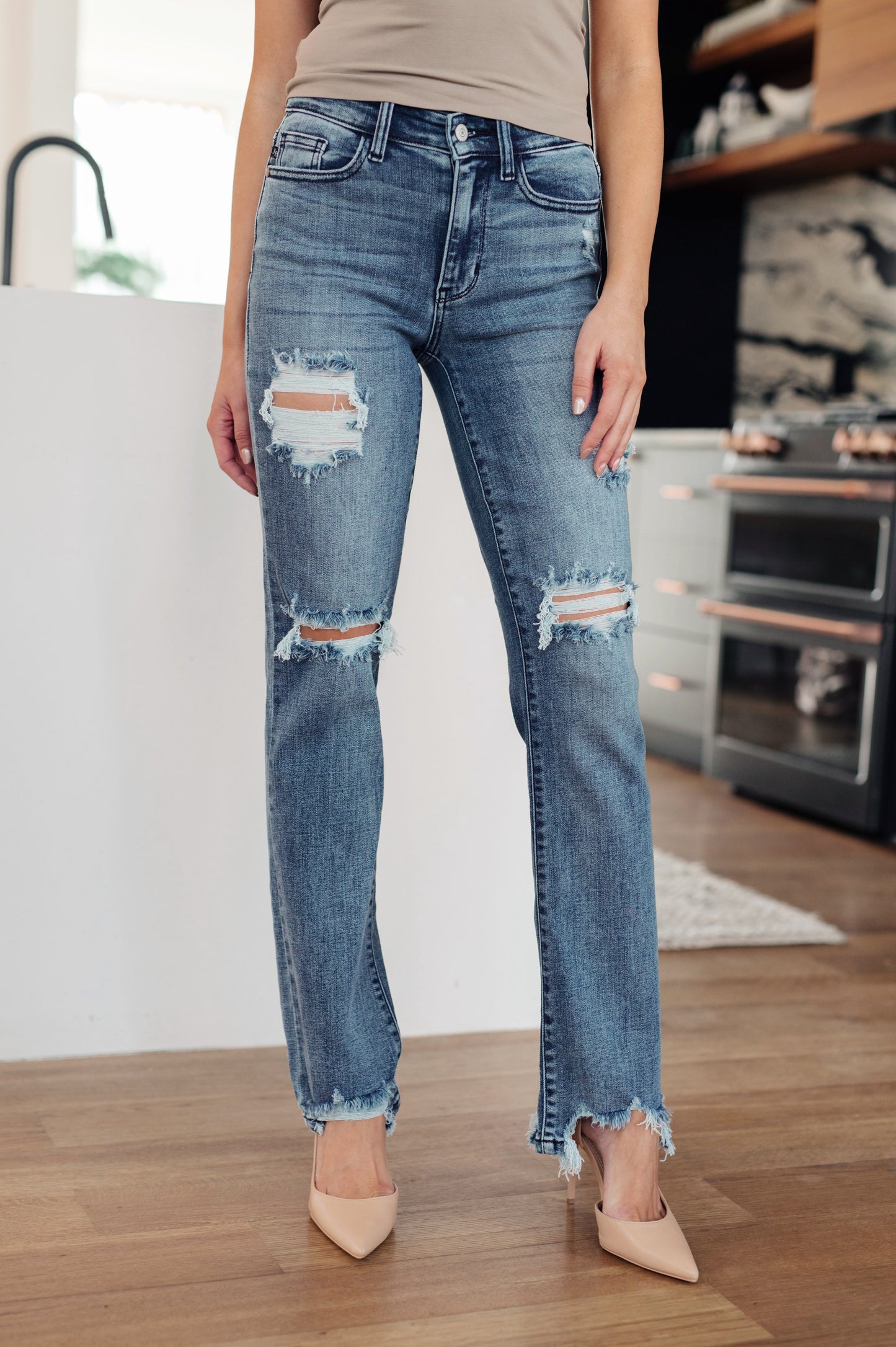 Medium wash mid-rise straight leg jeans with 4-way stretch for comfort. Features a five-pocket design, zipper fly, raw hem, and distressed details.