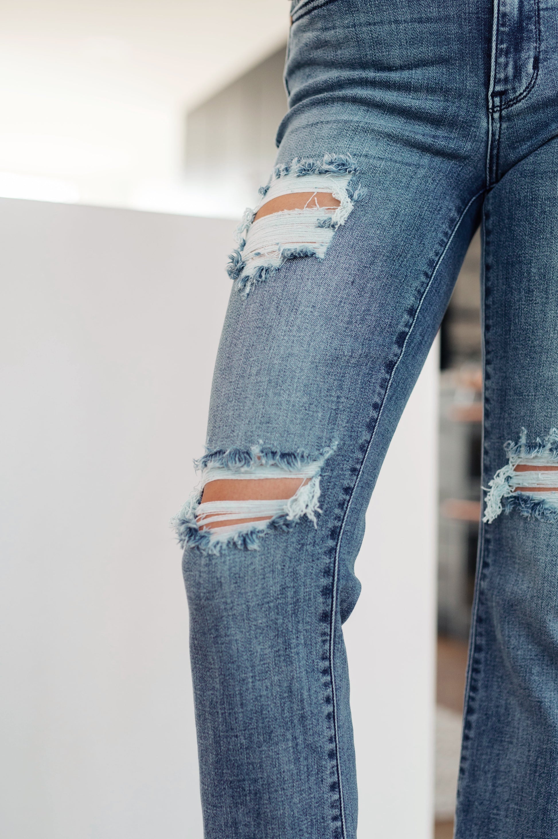 Medium wash mid-rise straight leg jeans with 4-way stretch for comfort. Features a five-pocket design, zipper fly, raw hem, and distressed details.