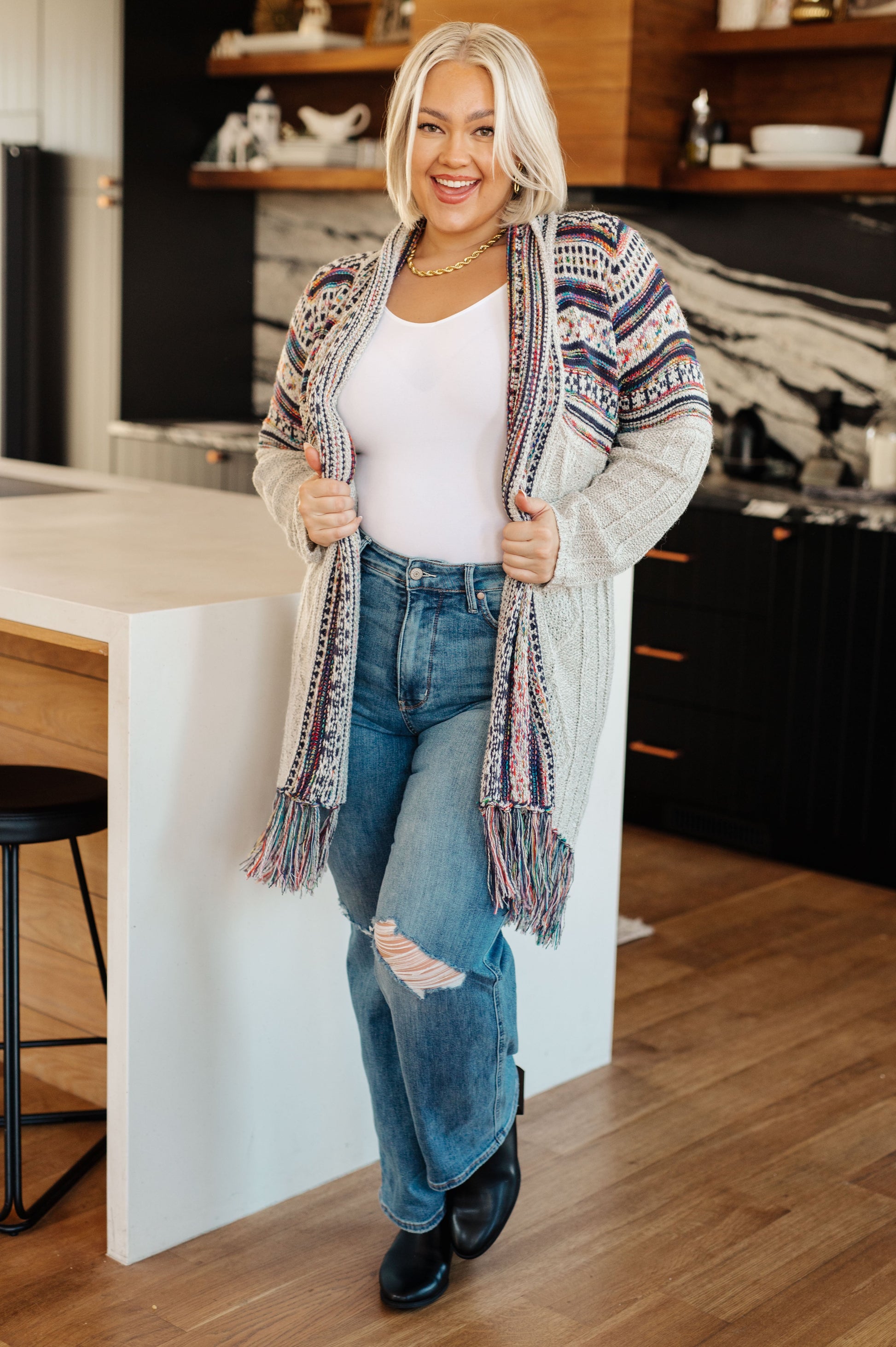 Women's cardigan with a shawl collar, geometric pattern, multi color, fringe trim, ribbed hem, and sweater knit fabric.