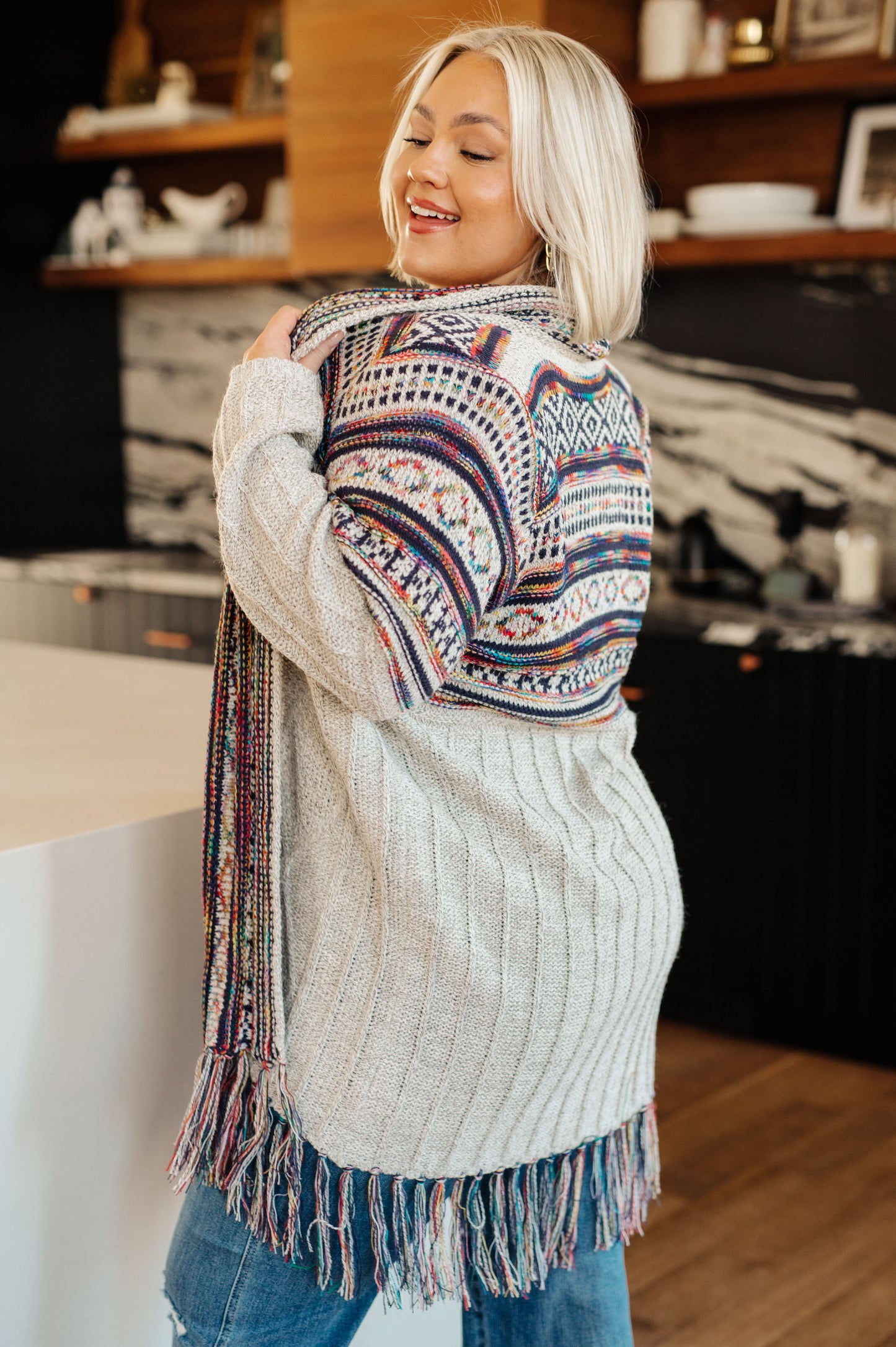 Women's cardigan with a shawl collar, geometric pattern, multi color, fringe trim, ribbed hem, and sweater knit fabric.