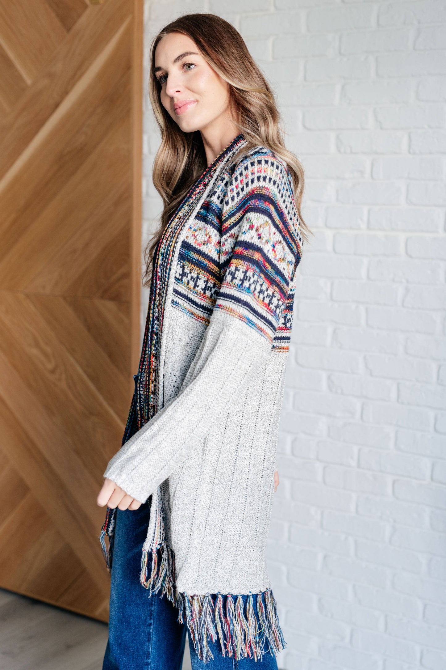 Women's cardigan with a shawl collar, geometric pattern, multi color, fringe trim, ribbed hem, and sweater knit fabric.