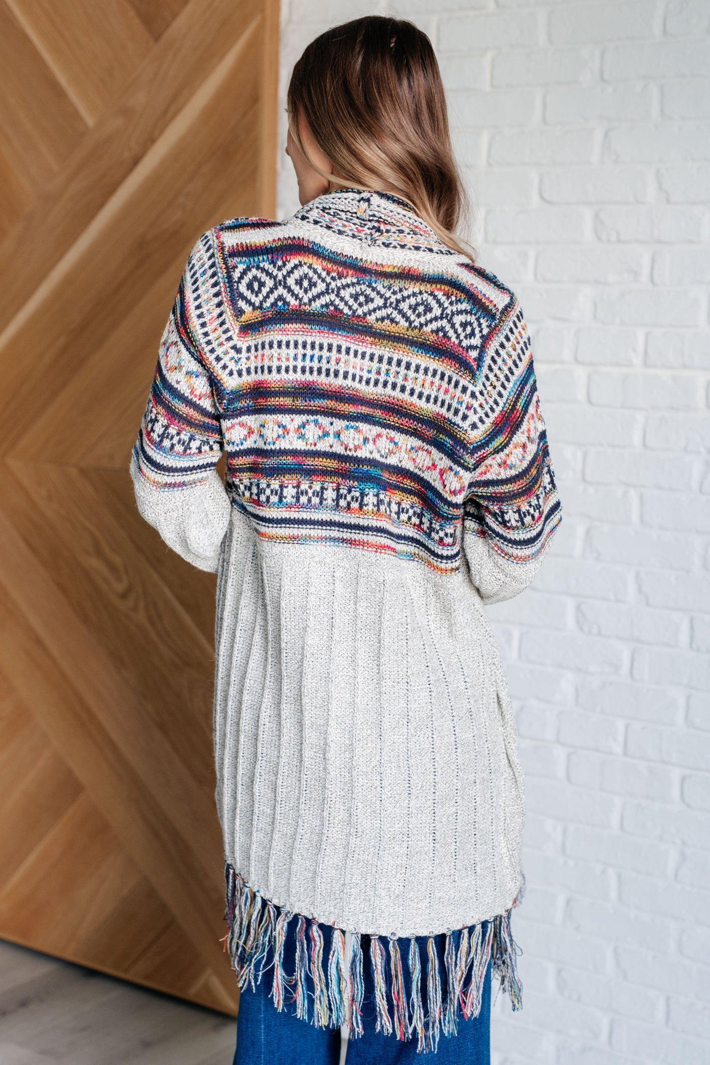 Women's cardigan with a shawl collar, geometric pattern, multi color, fringe trim, ribbed hem, and sweater knit fabric.