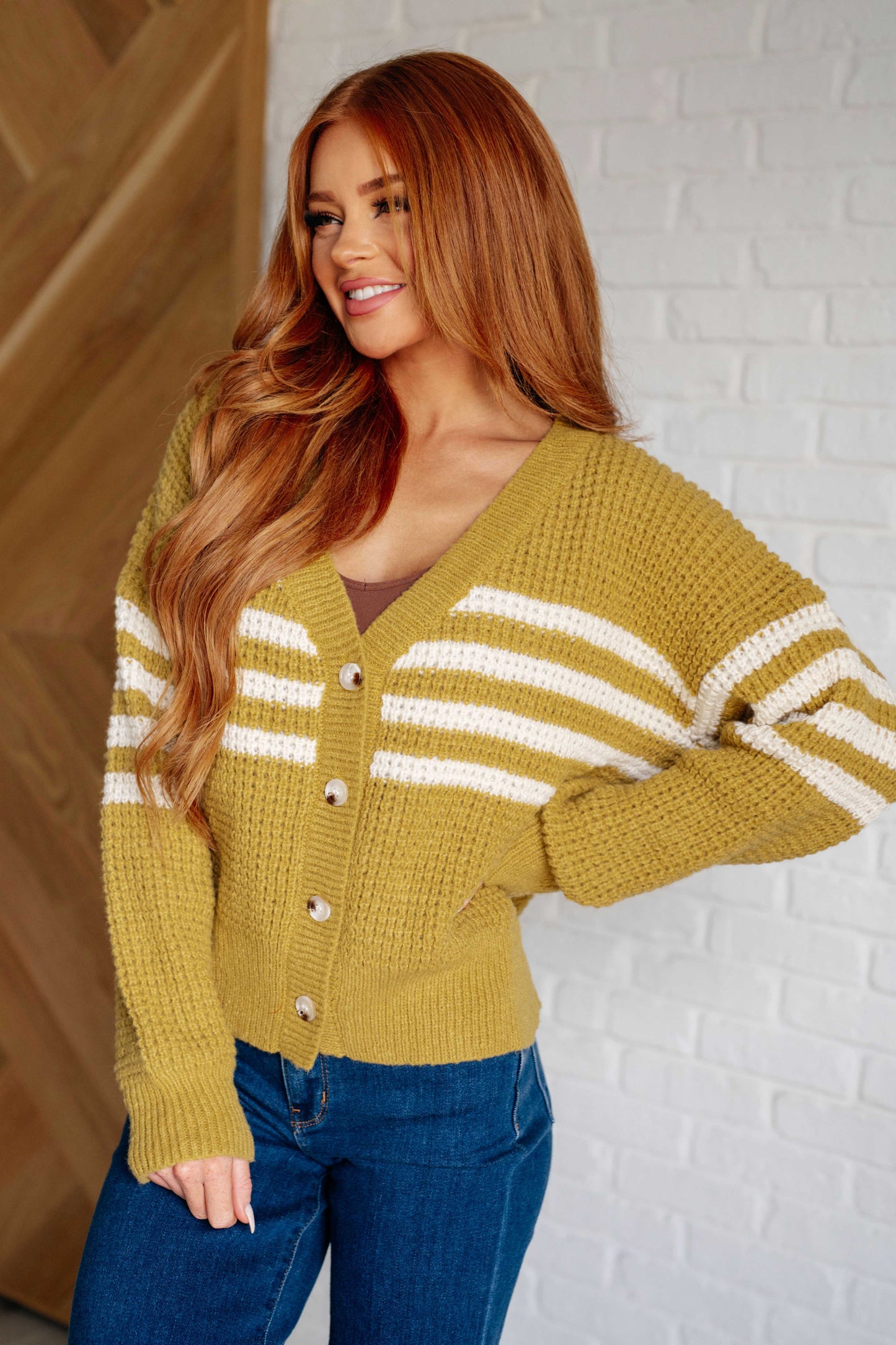 Women's mustard cardigan with white stripes made from waffle sweater knit fabric, V-neck, long sleeves, ribbed knit trim, and button front closure.