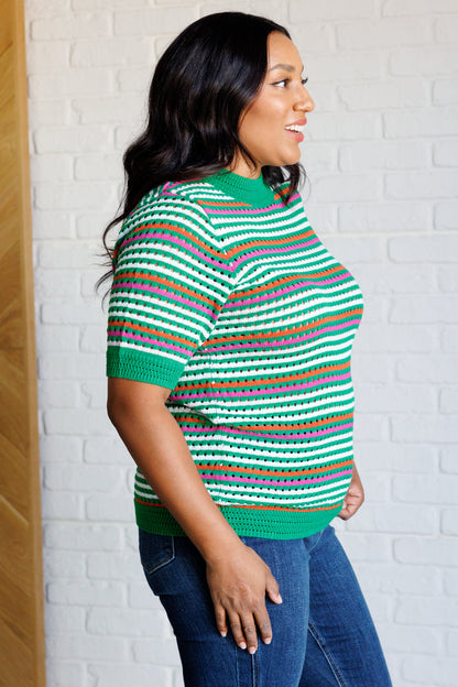 Side view of a plus size model wearing the Sitarah Knit Striped Top in green with orange, white, and pink stripes, featuring a high-stretch sweater knit, round neckline, and half sleeves for a trendy and comfortable fit.