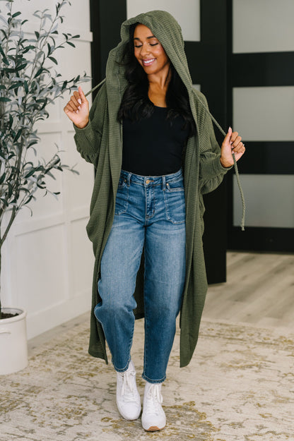 Model wearing Remington Hooded Cardigan in olive with hood up and open front style.