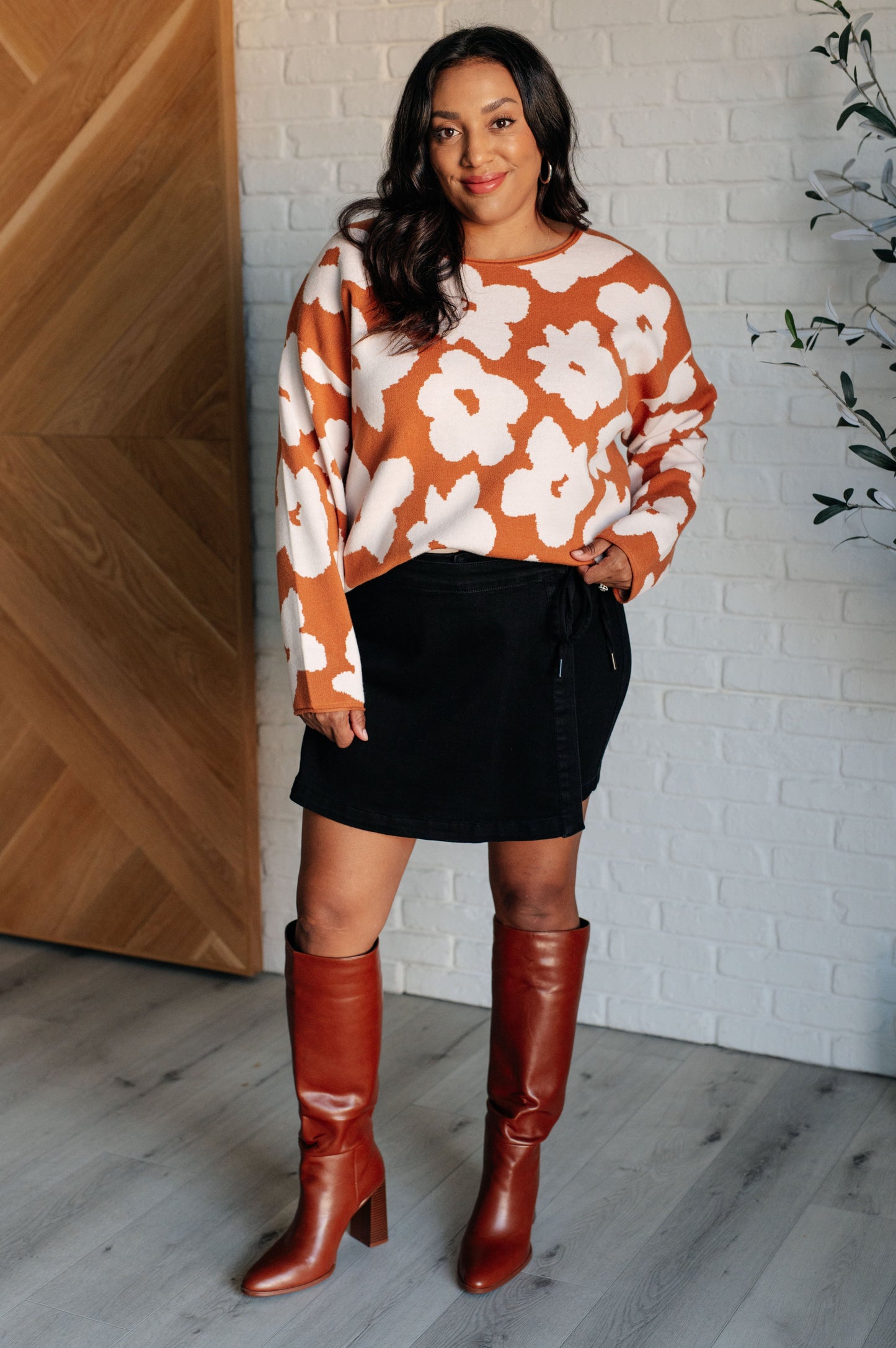 A rust-colored sweater made from mid-weight knit fabric featuring a white floral print. The design includes a round neckline, long drop-shoulder sleeves, and a relaxed fit silhouette.