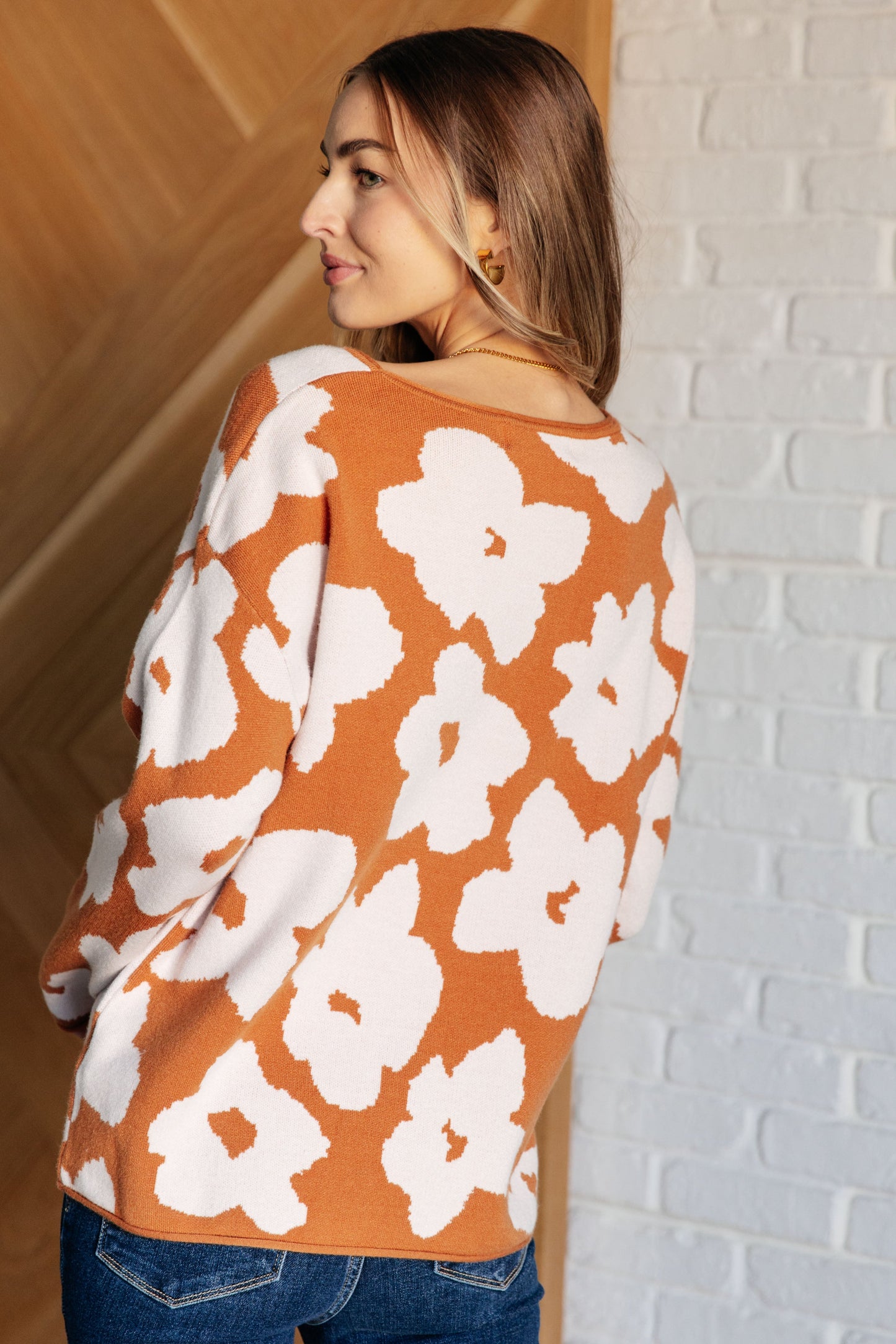 A rust-colored sweater made from mid-weight knit fabric featuring a white floral print. The design includes a round neckline, long drop-shoulder sleeves, and a relaxed fit silhouette.