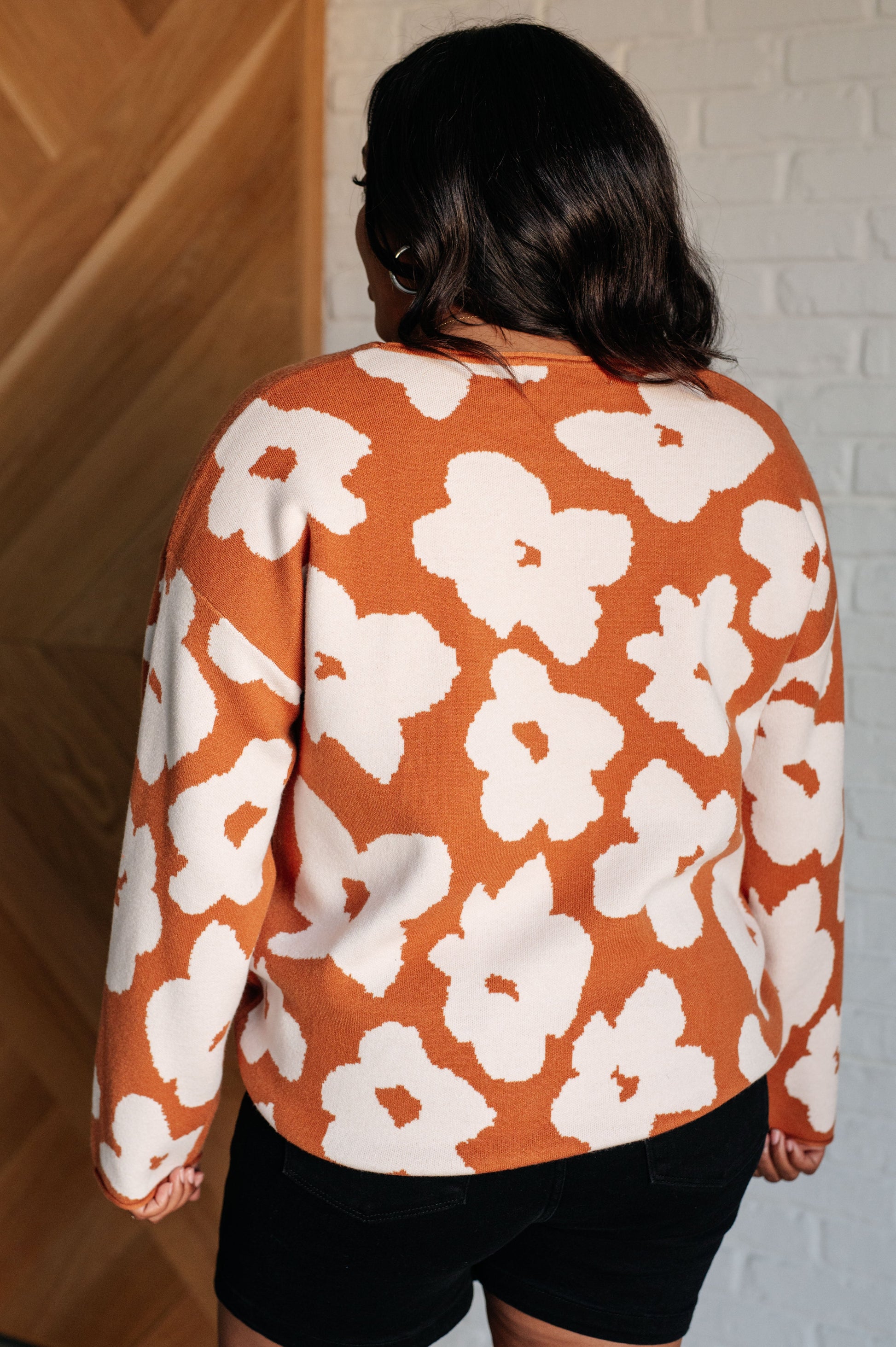 A rust-colored sweater made from mid-weight knit fabric featuring a white floral print. The design includes a round neckline, long drop-shoulder sleeves, and a relaxed fit silhouette.