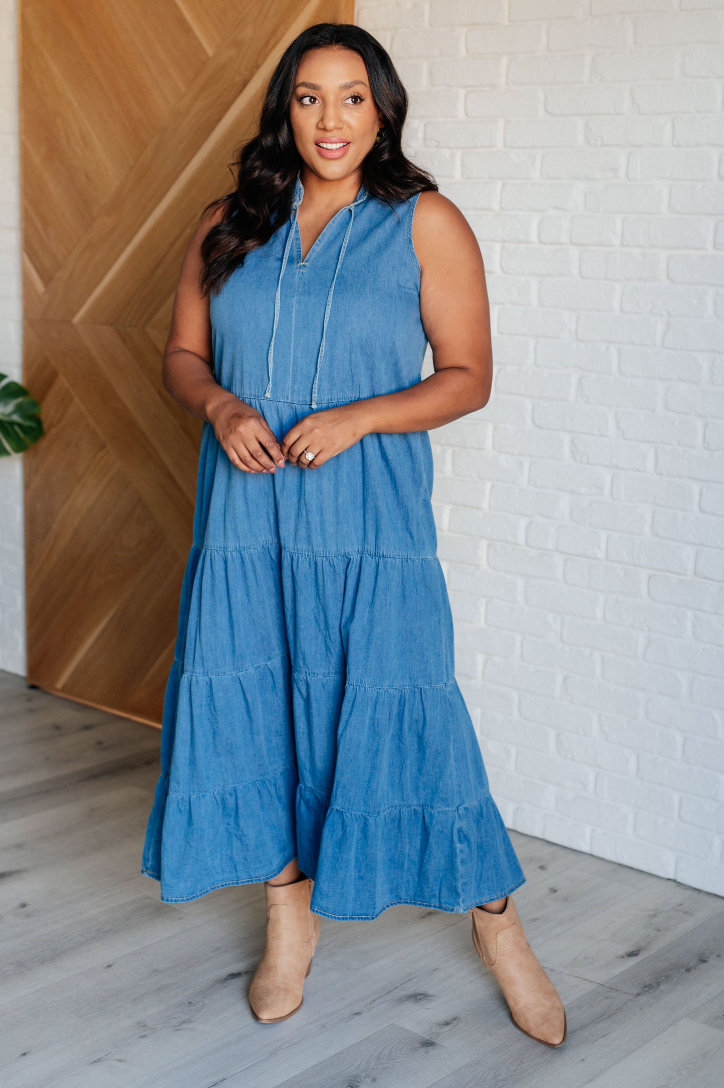 Chambray denim maxi dress featuring a V-neckline with functional neck ties, a tiered skirt, and a sleeveless design. Lightweight and flowy.