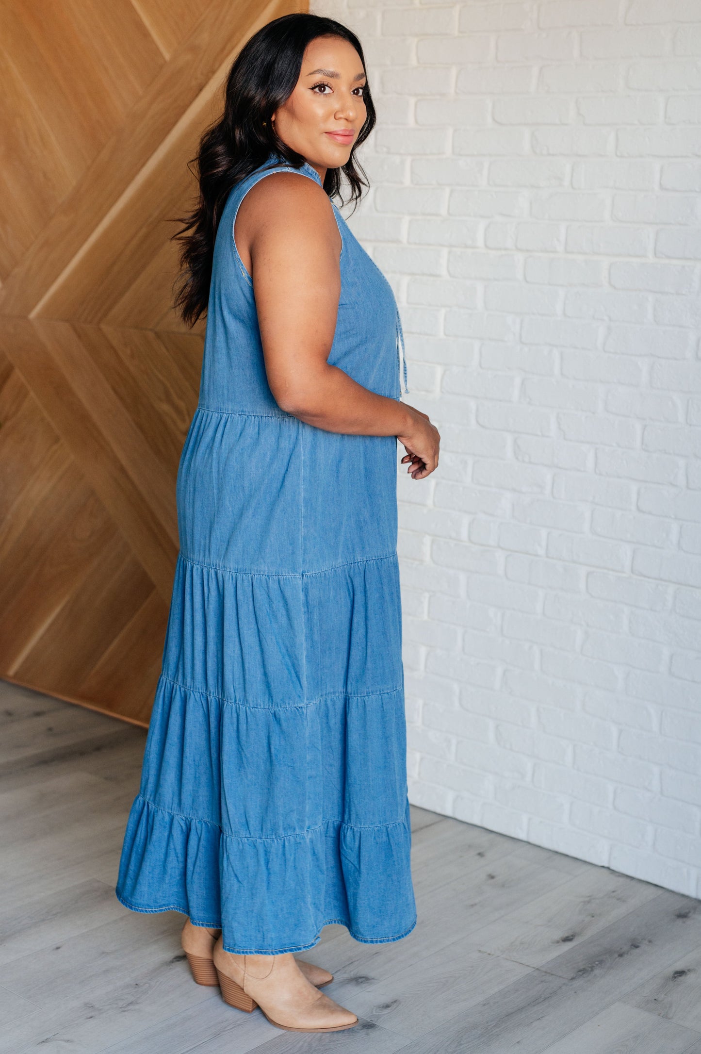 Chambray denim maxi dress featuring a V-neckline with functional neck ties, a tiered skirt, and a sleeveless design. Lightweight and flowy.