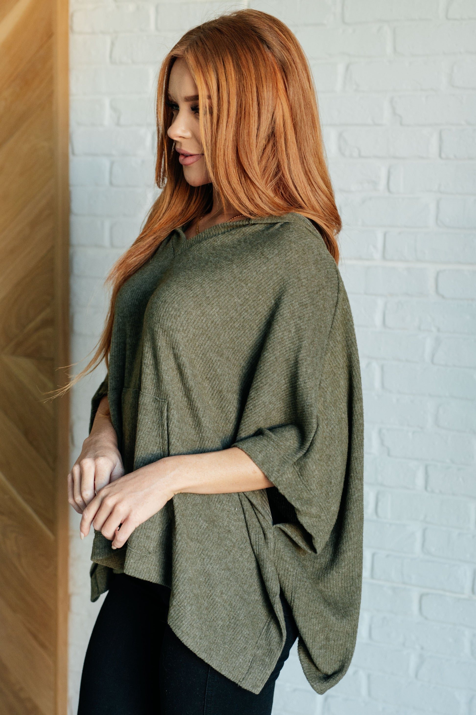 Women's olive poncho with a hood, kangaroo pocket, and lightweight ribbed jersey knit fabric, perfect for layering and casual wear.