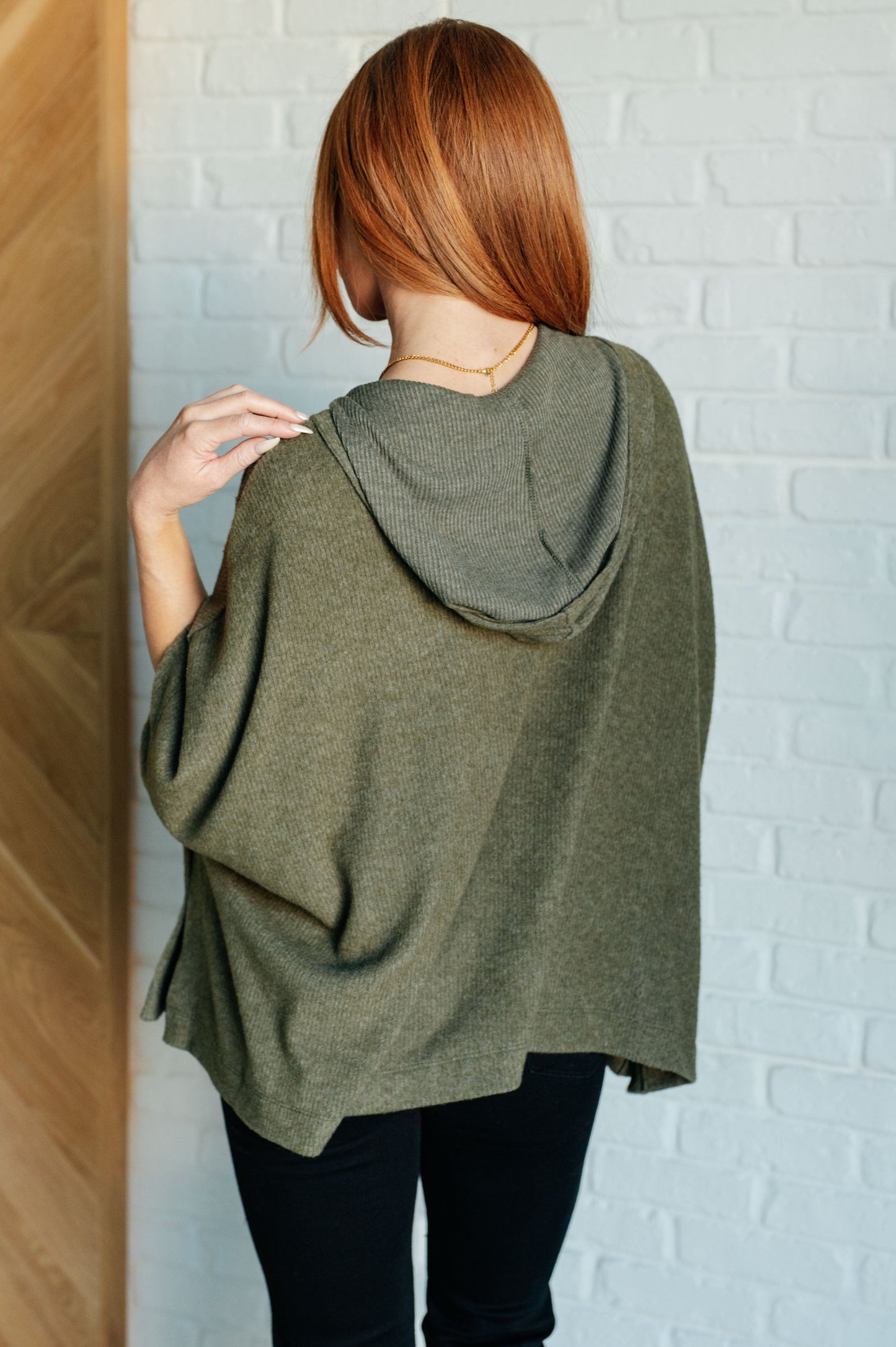 Women's olive poncho with a hood, kangaroo pocket, and lightweight ribbed jersey knit fabric, perfect for layering and casual wear.