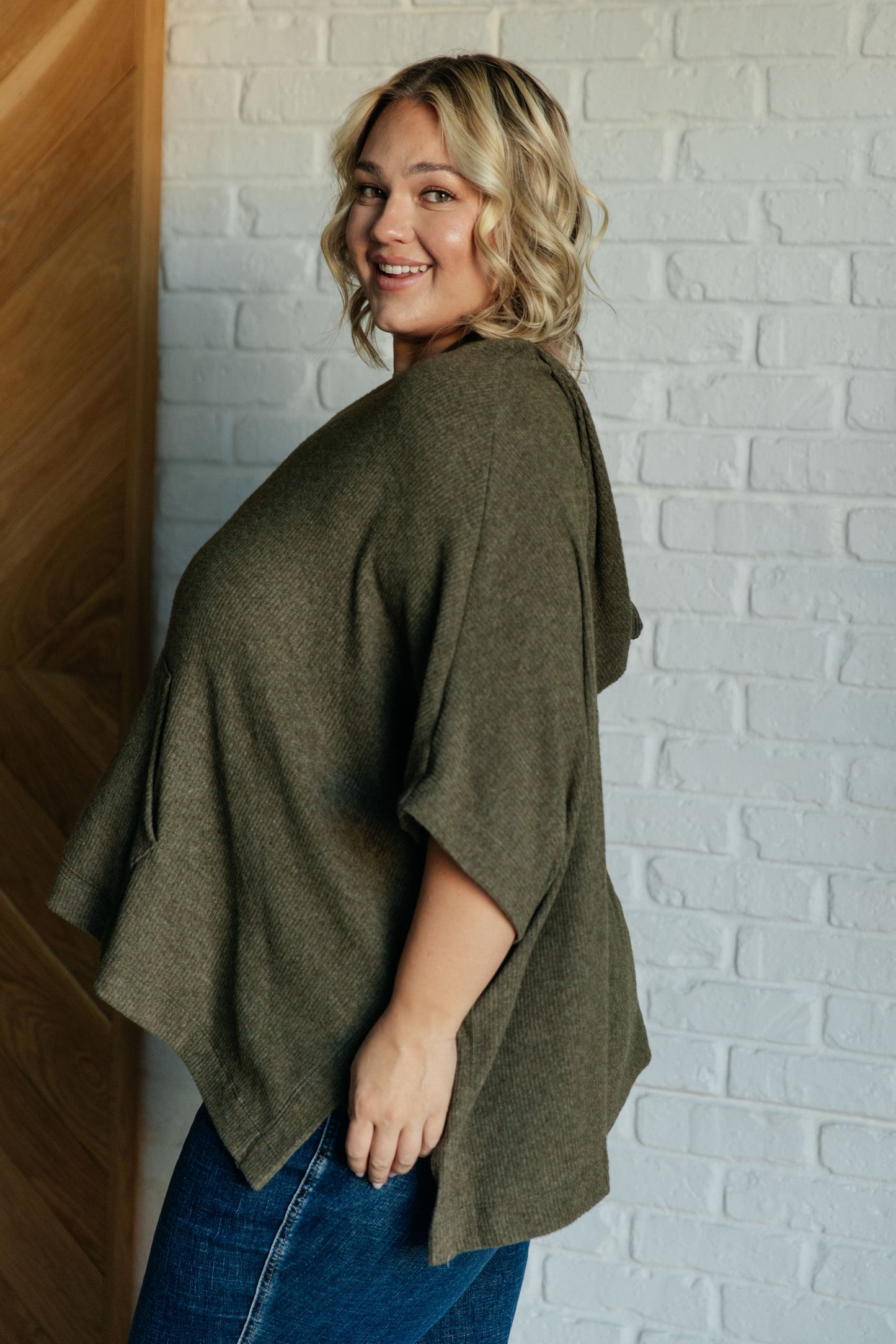 Women's olive poncho with a hood, kangaroo pocket, and lightweight ribbed jersey knit fabric, perfect for layering and casual wear.