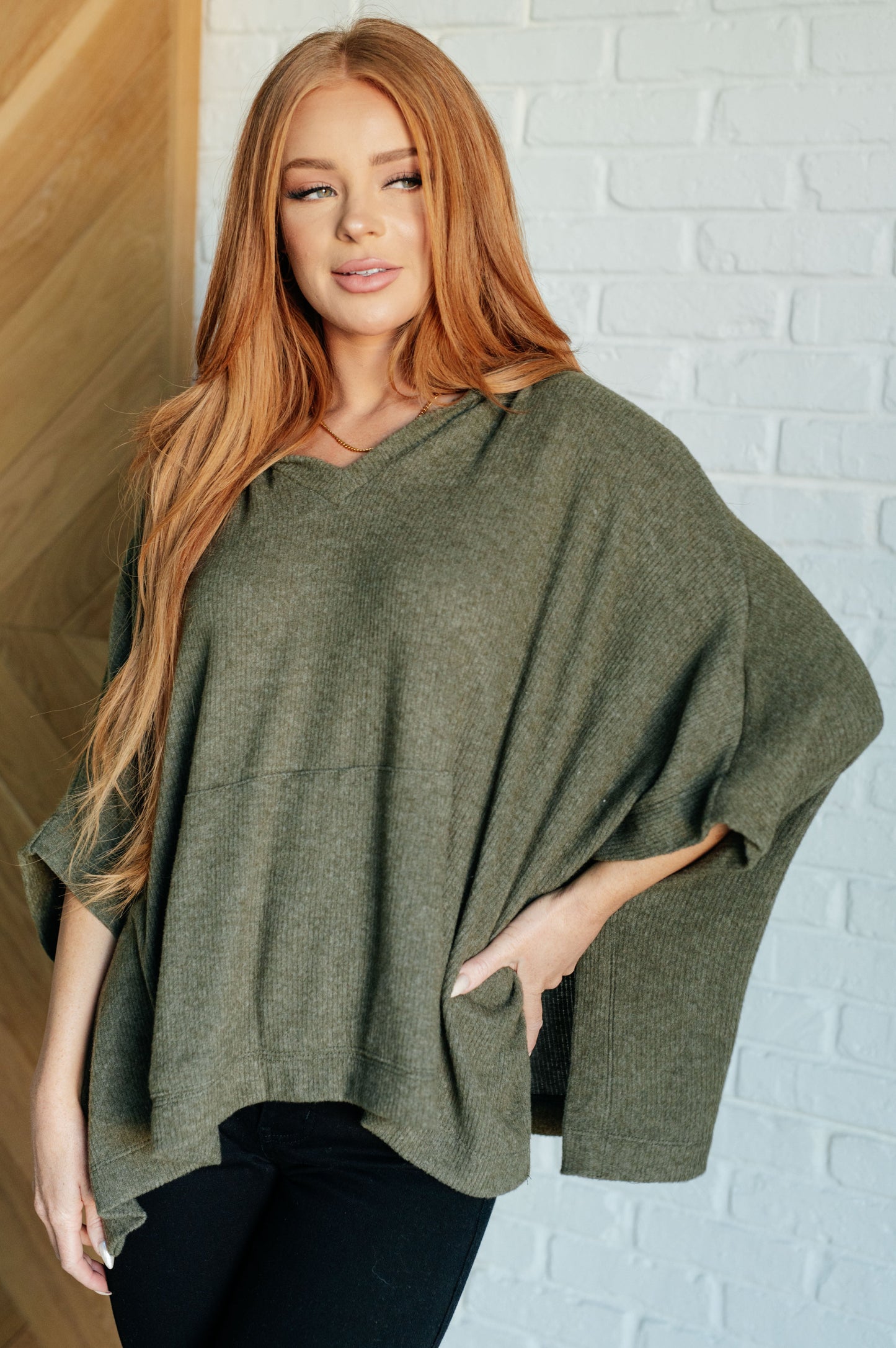 Women's olive poncho with a hood, kangaroo pocket, and lightweight ribbed jersey knit fabric, perfect for layering and casual wear.