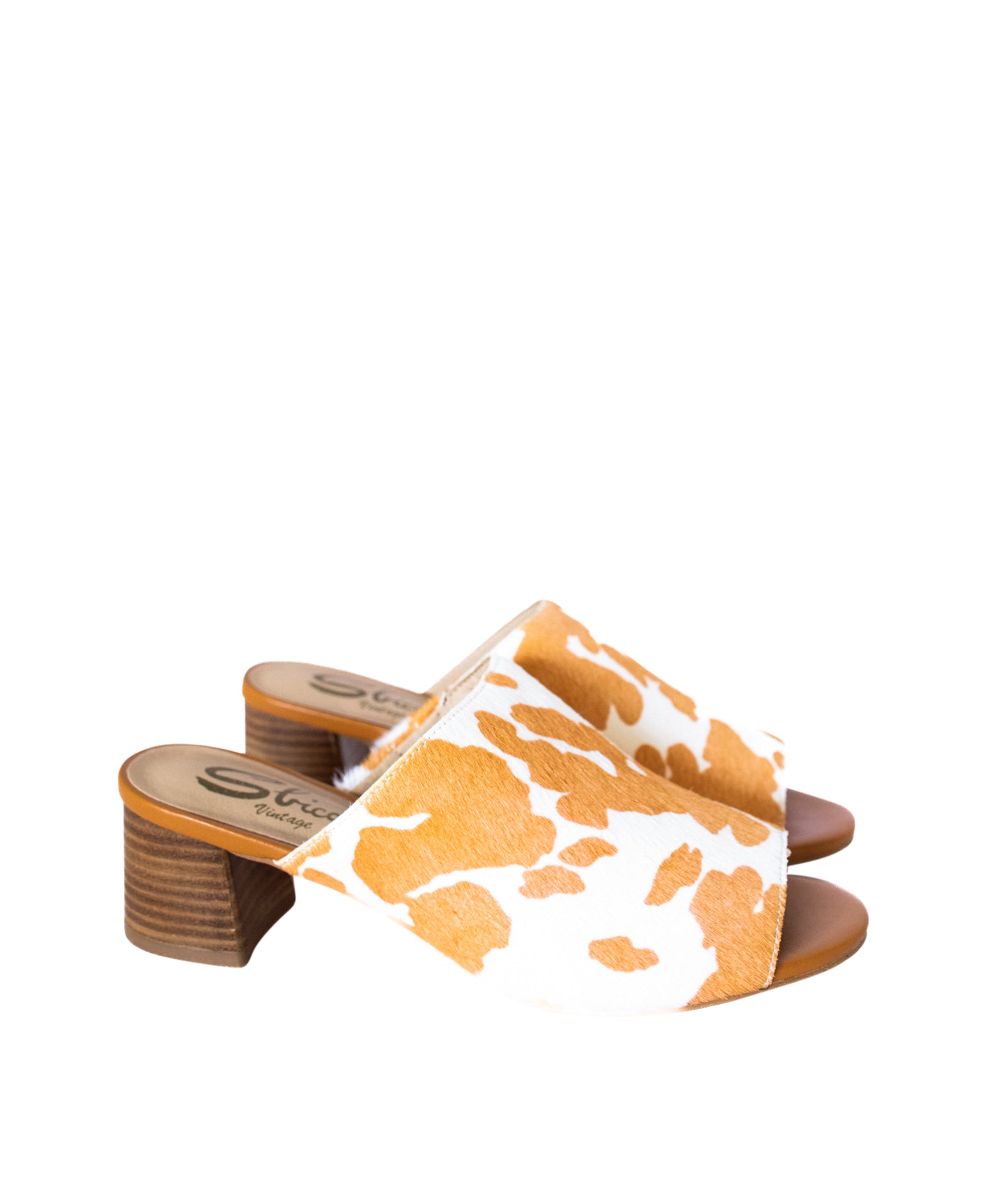 Tan and white cow print mule shoes for women, featuring a genuine calf-hair upper, synthetic lining, padded insole, and internal elastic gore for comfort. Designed with a low stacked leather heel, these slip-on mules are perfect for pairing with jeans, jumpsuits, or other outfits to add a playful, bold touch.