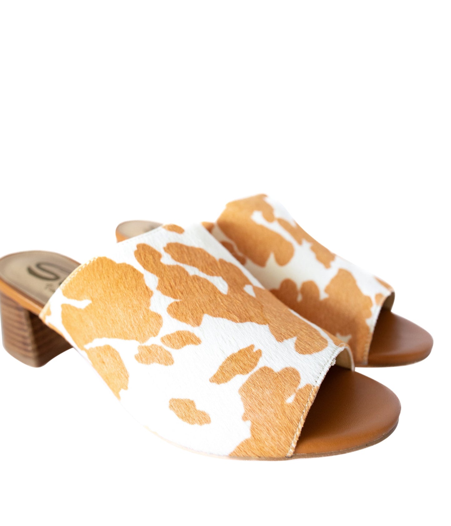 Tan and white cow print mule shoes for women, featuring a genuine calf-hair upper, synthetic lining, padded insole, and internal elastic gore for comfort. Designed with a low stacked leather heel, these slip-on mules are perfect for pairing with jeans, jumpsuits, or other outfits to add a playful, bold touch.