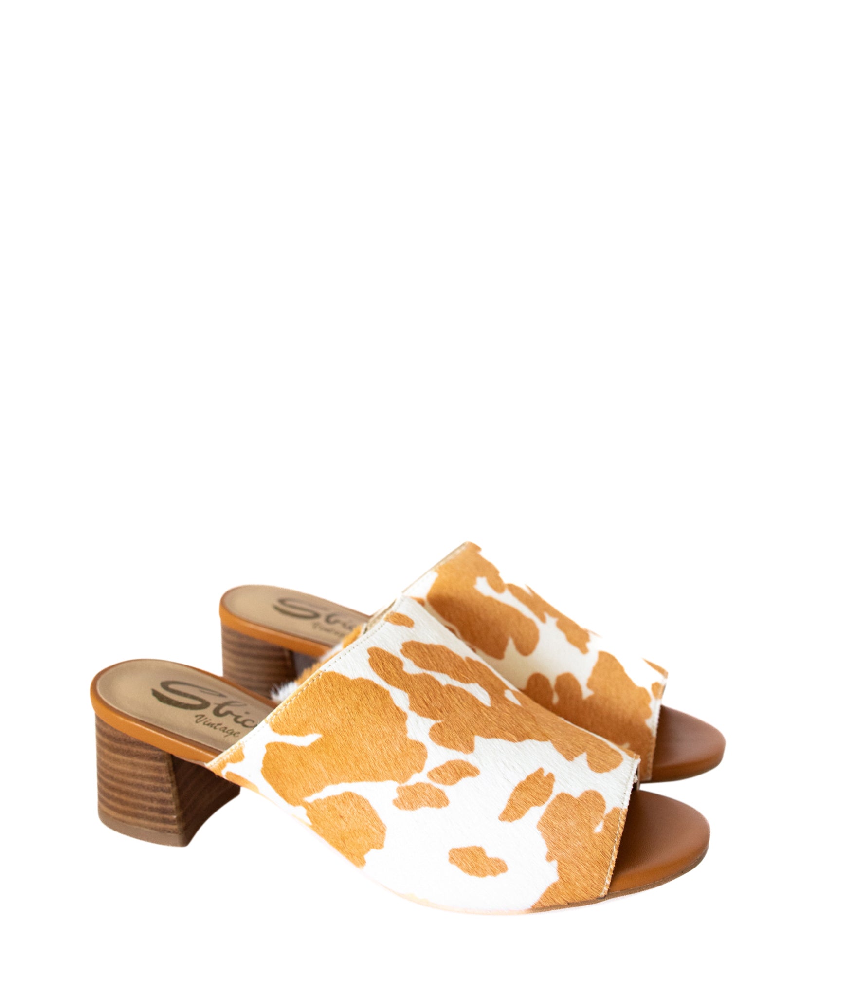 Tan and white cow print mule shoes for women, featuring a genuine calf-hair upper, synthetic lining, padded insole, and internal elastic gore for comfort. Designed with a low stacked leather heel, these slip-on mules are perfect for pairing with jeans, jumpsuits, or other outfits to add a playful, bold touch.