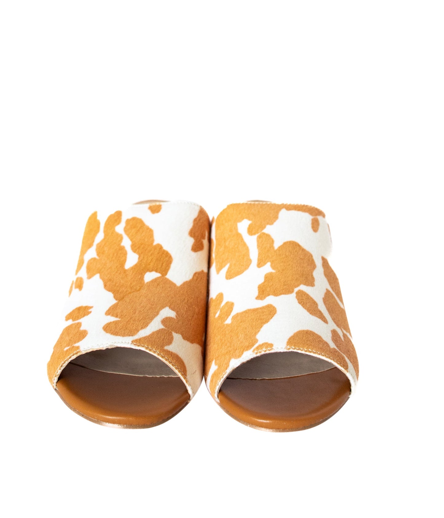 Tan and white cow print mule shoes for women, featuring a genuine calf-hair upper, synthetic lining, padded insole, and internal elastic gore for comfort. Designed with a low stacked leather heel, these slip-on mules are perfect for pairing with jeans, jumpsuits, or other outfits to add a playful, bold touch.