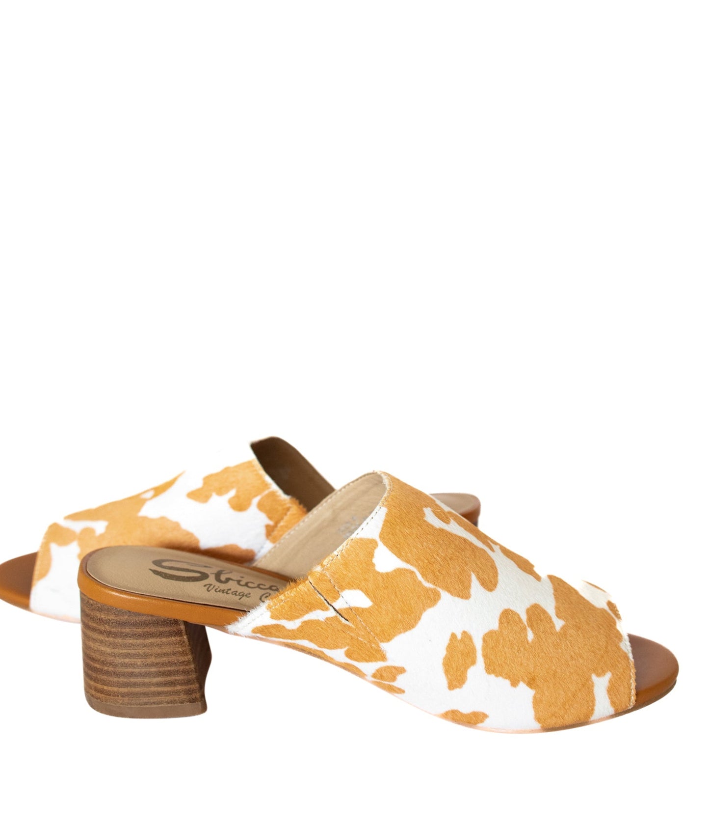 Tan and white cow print mule shoes for women, featuring a genuine calf-hair upper, synthetic lining, padded insole, and internal elastic gore for comfort. Designed with a low stacked leather heel, these slip-on mules are perfect for pairing with jeans, jumpsuits, or other outfits to add a playful, bold touch.